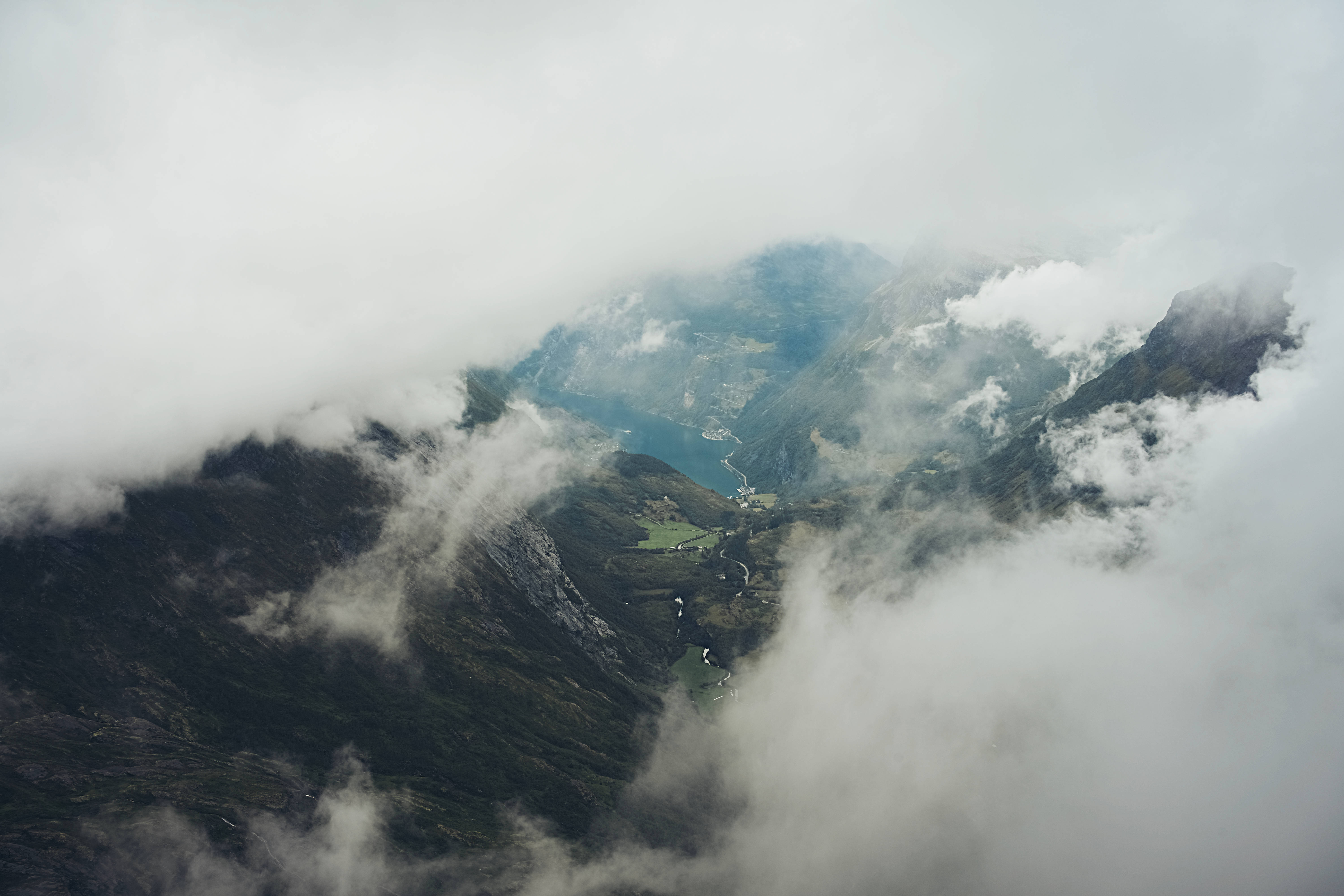 Norway 桌布 壁紙 — 雲霧繚繞的峽灣，坐落於高聳的山峰之間，雲朵在山峰和山谷間盤旋。