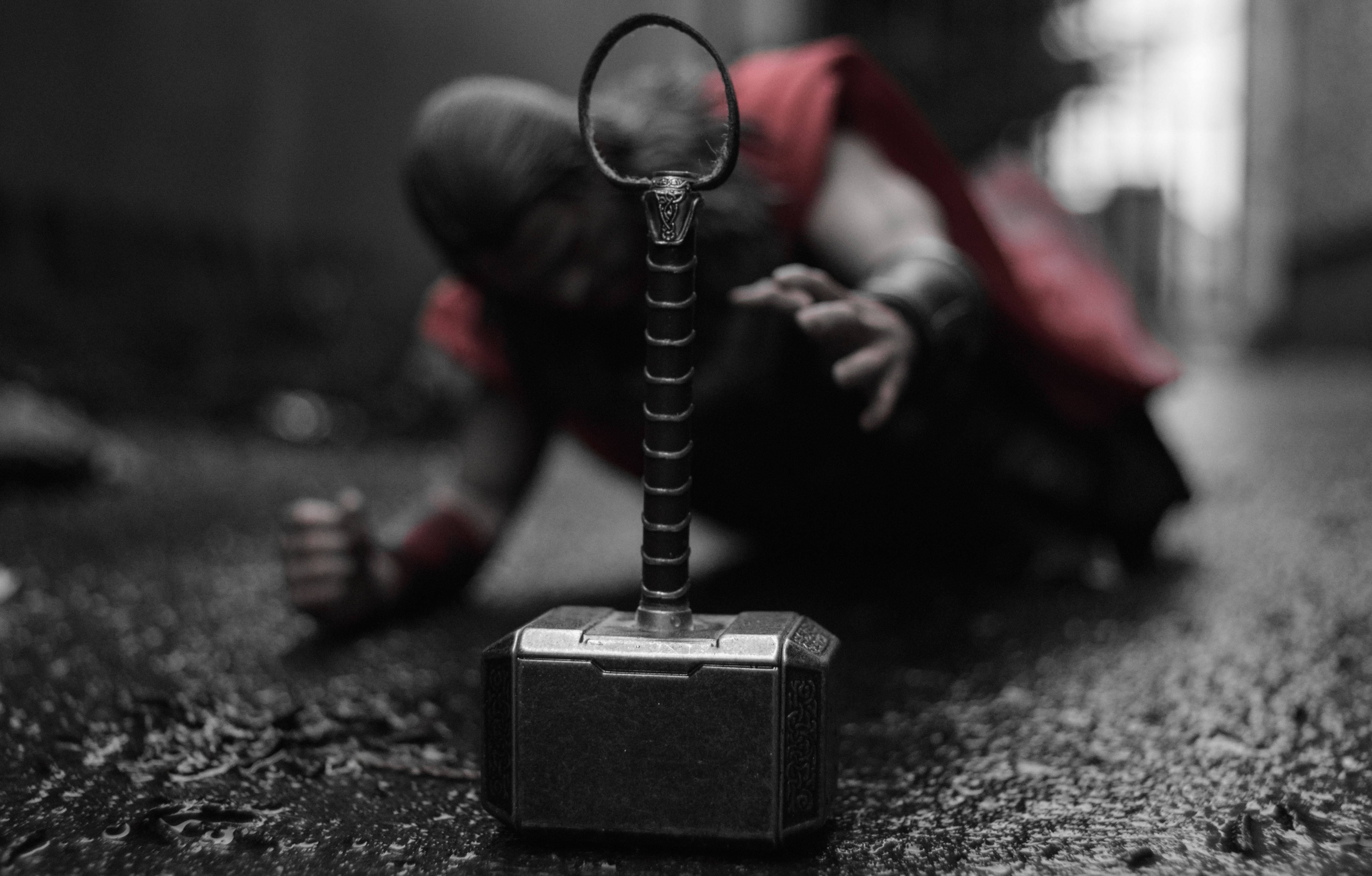 Thors Hammer 桌布 壁紙 — 雷神之鎚妙爾尼爾的特寫，直立於濕漉漉的路面上，一個模糊的紅色身影在其後爬行。