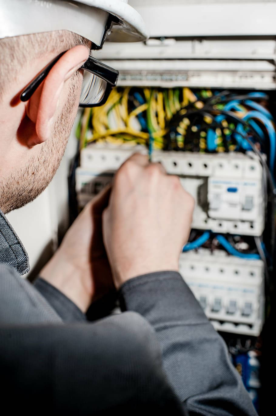 professional 桌布 壁紙 — 電工戴著頭盔和眼鏡，仔細地在一個充滿彩色電線和斷路器的面板上工作的特寫。