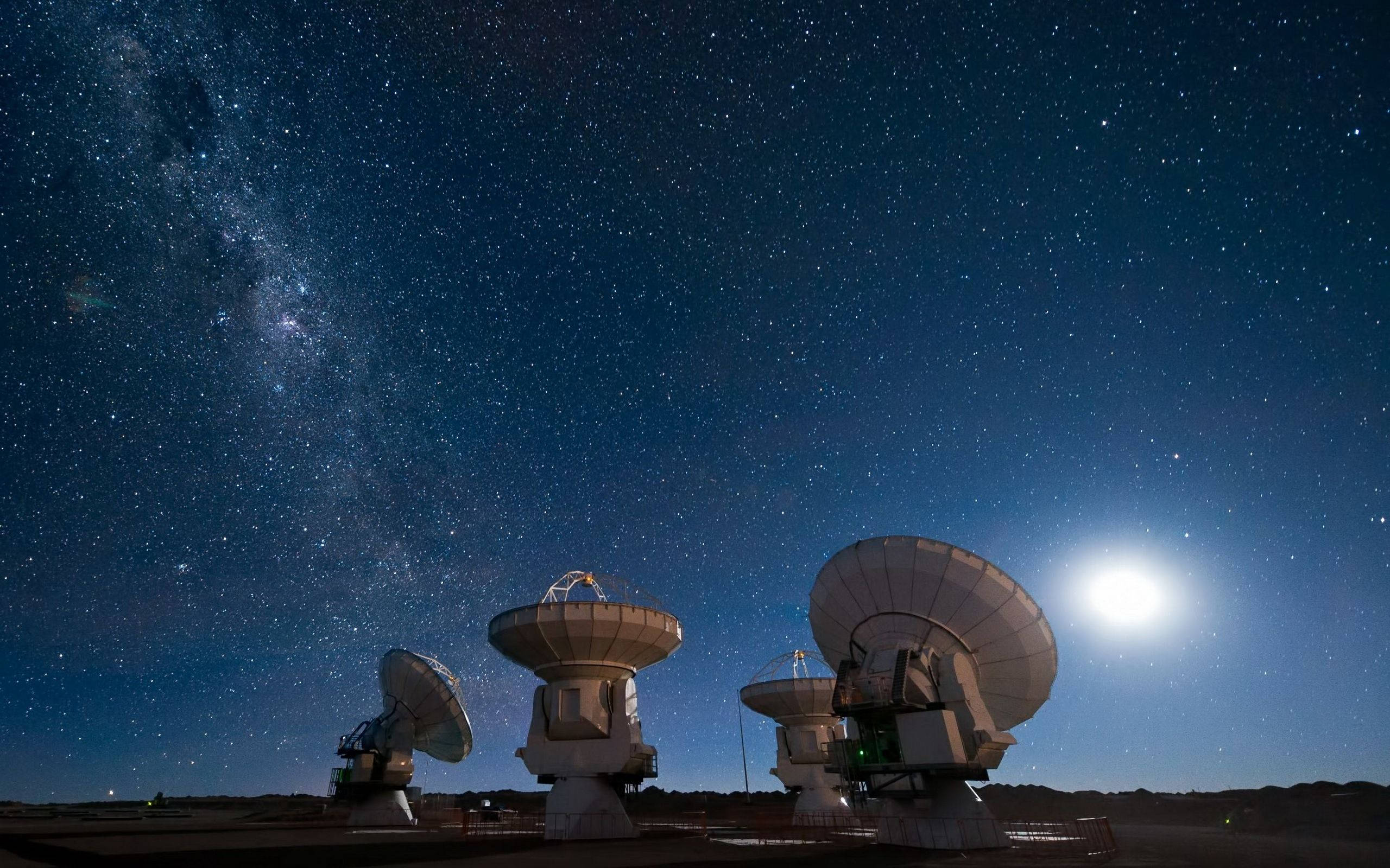 Telescope 桌布 壁紙 — 電波望遠鏡在繁星點點的夜空下呈現剪影，銀河和明亮的月亮在上方閃耀。