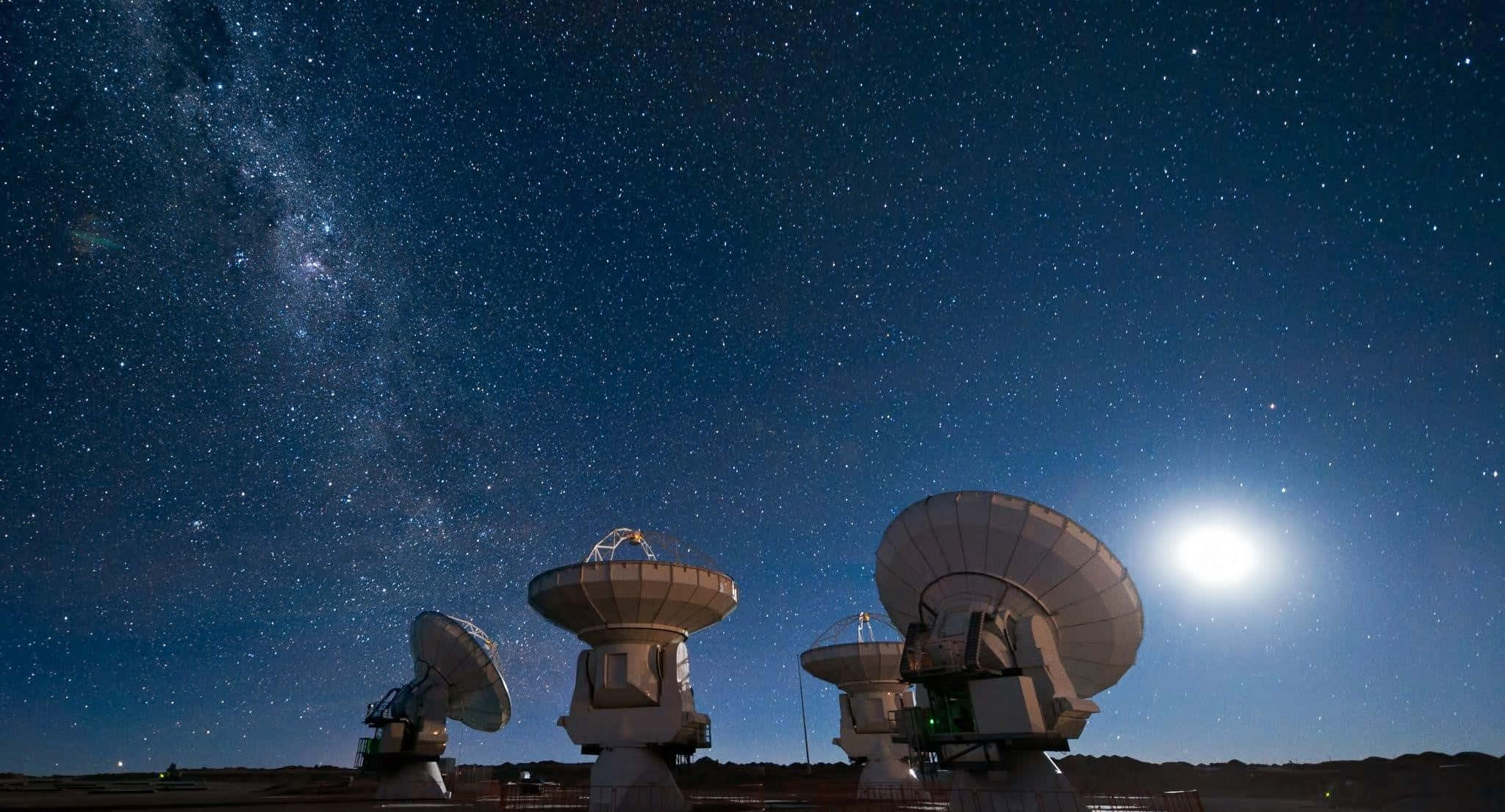 Satellite 桌布 壁紙 — 電波望遠鏡在繁星點點的夜空下呈現剪影，銀河和明亮的月亮在上方閃耀。