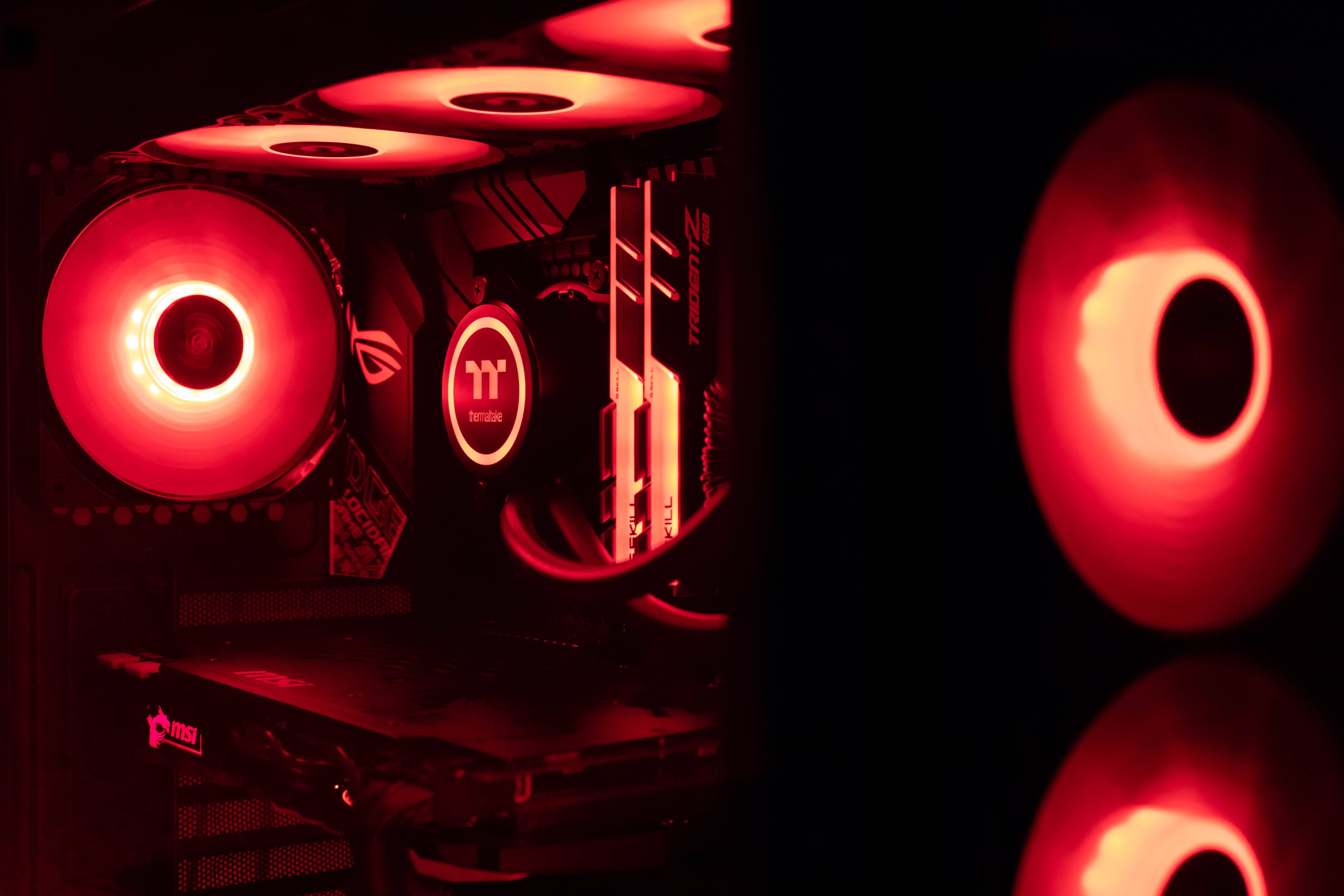 msi 2560x1080 桌布 壁紙 — 電腦內部組件特寫，在黑暗背景下沐浴在發光的紅色 LED 風扇中。