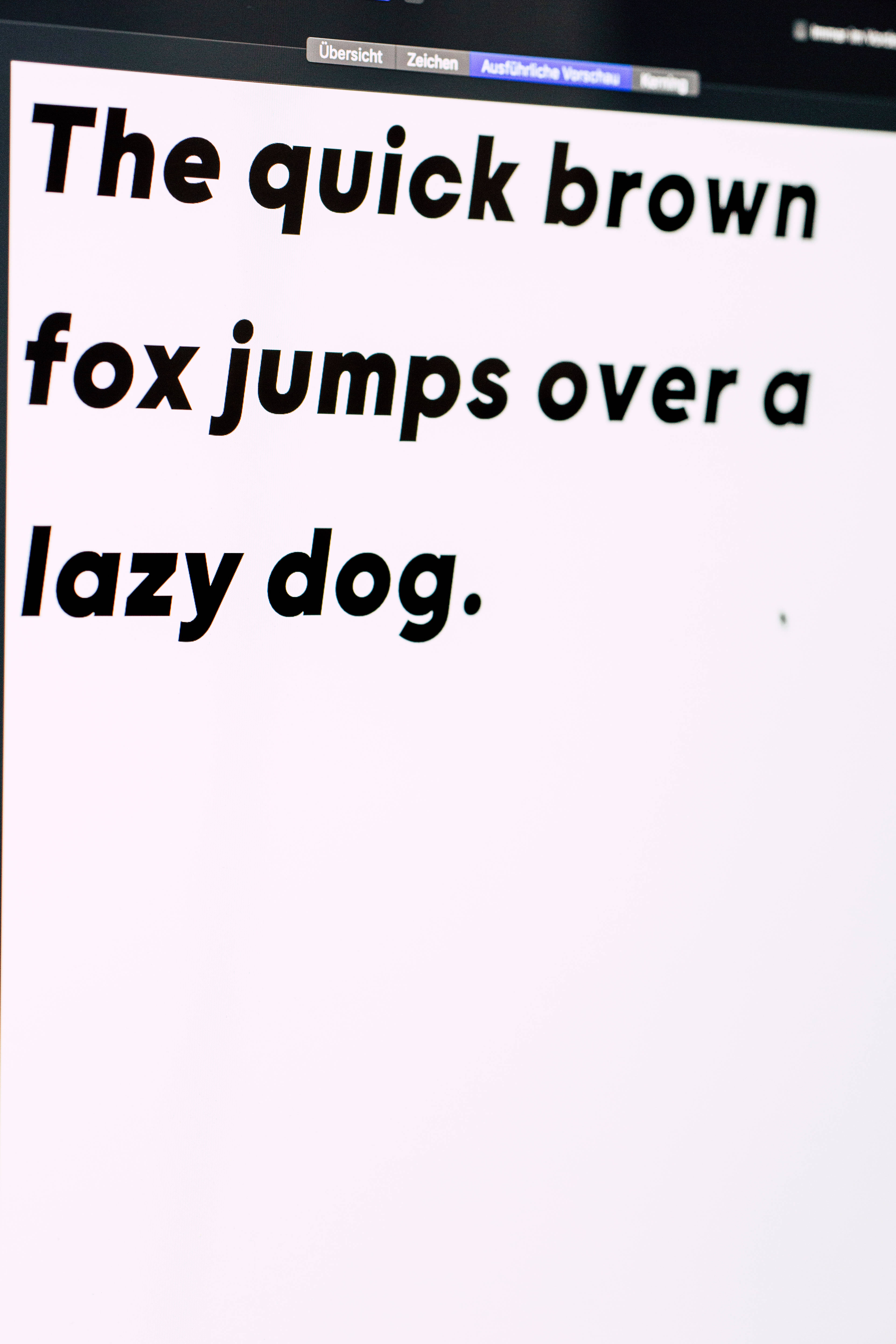 字型 桌布 壁紙 — 電腦螢幕特寫，顯示全字母句「The quick brown fox jumps over a lazy dog」，以粗體黑色文字呈現。