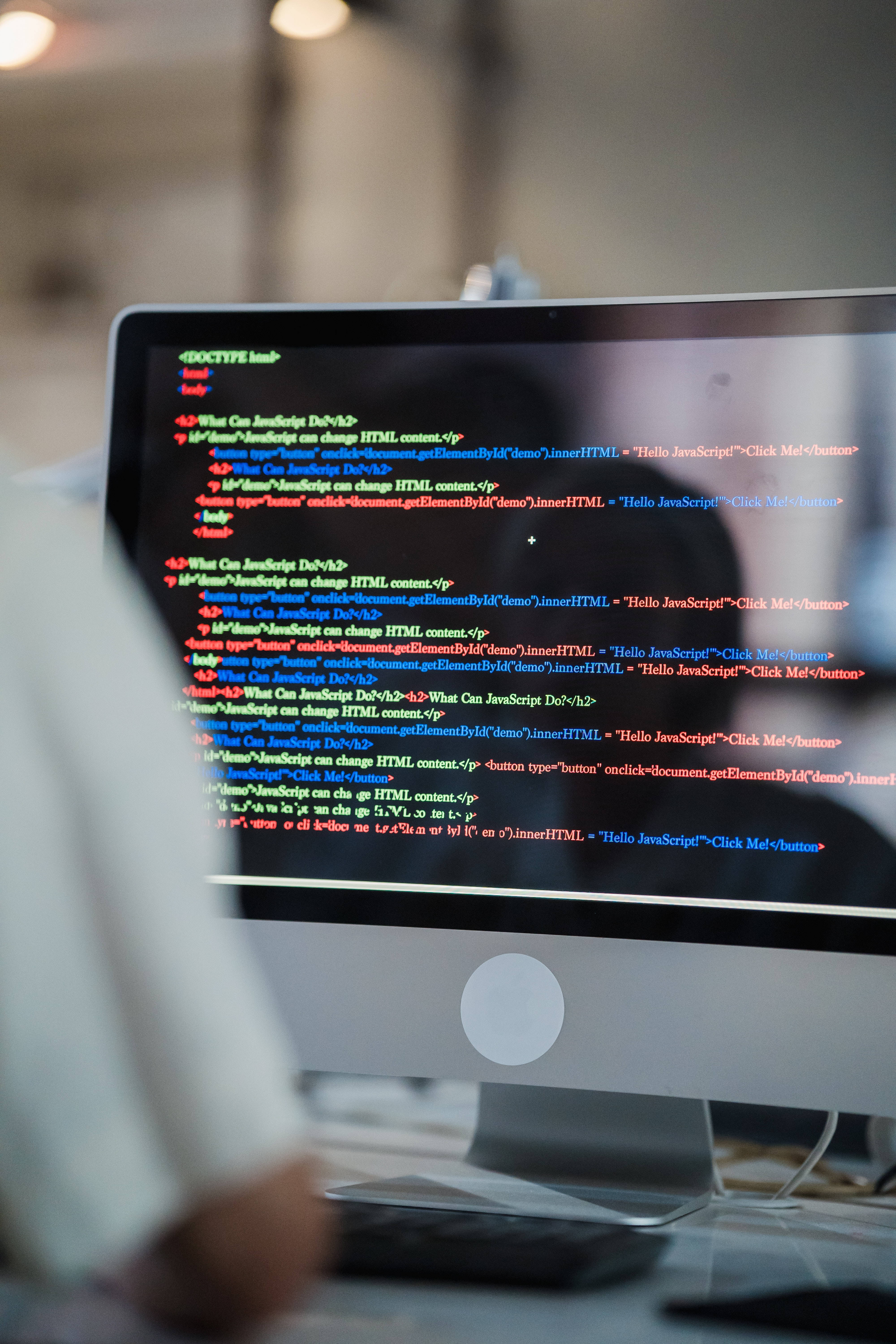 Computer Screen 桌布 壁紙 — 電腦顯示器特寫，顯示色彩繽紛的JavaScript程式碼，背景為模糊的辦公室。