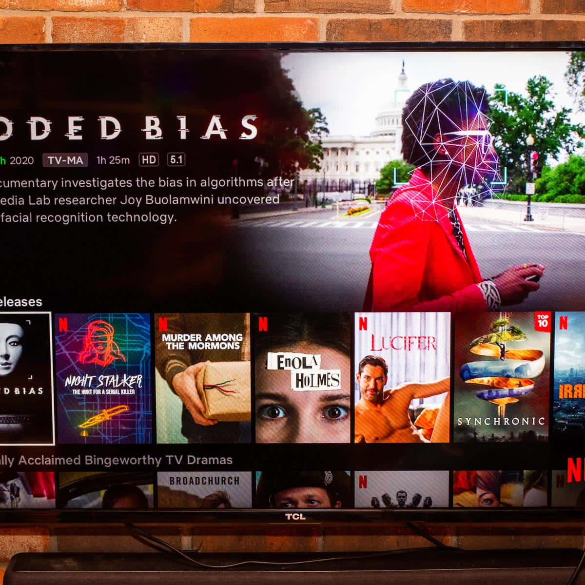 Netflix 桌布 壁紙 — 電視螢幕顯示Netflix介面，播放關於演算法偏見的紀錄片，畫面中有一個人穿著紅色外套，帶有臉部辨識疊加層，背景是國會大廈。