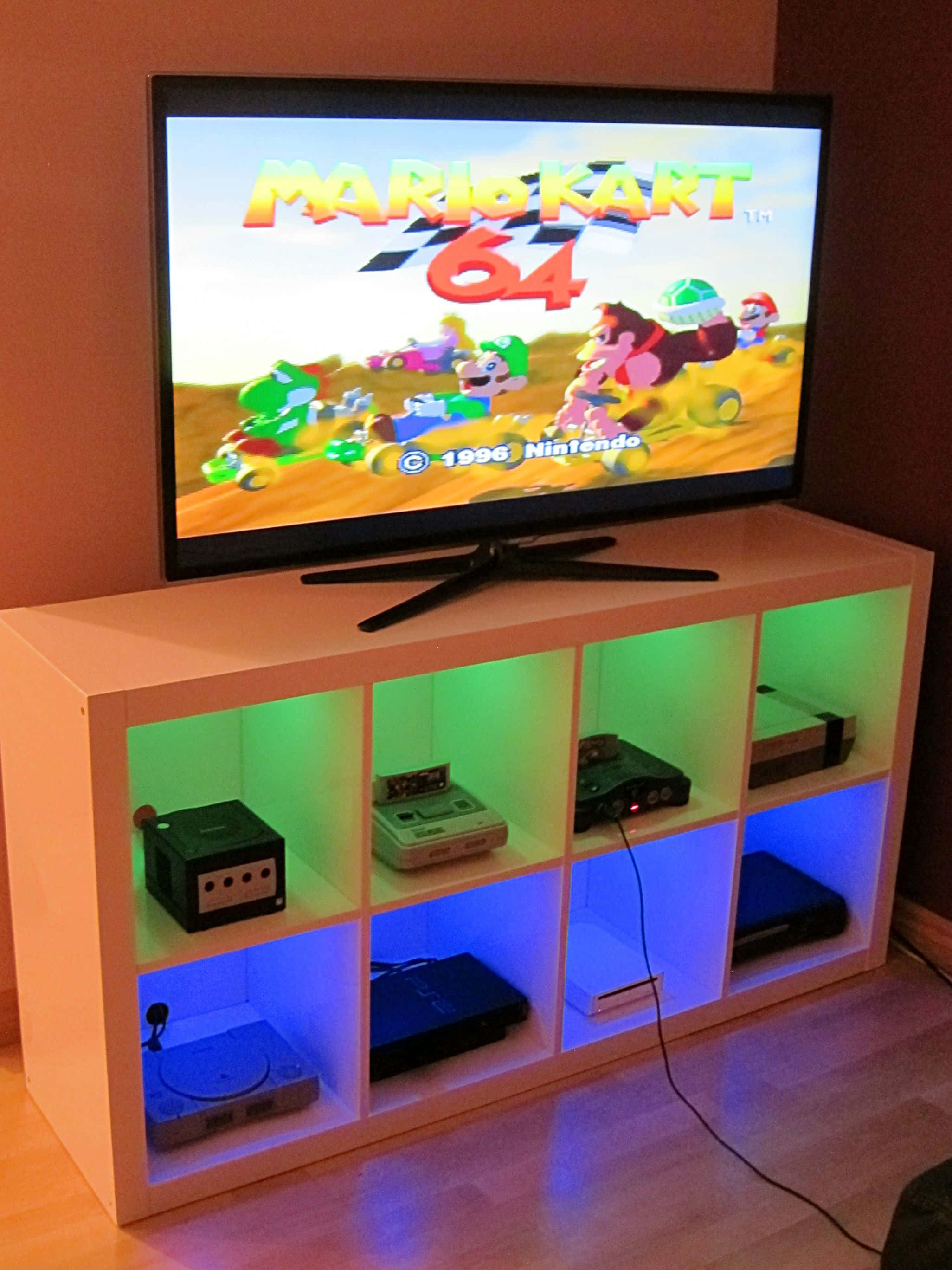Game Console Emulators 桌布 壁紙 — 電視顯示瑪利歐賽車64，而彩色LED燈照亮白色立方體媒體櫃中的復古遊戲機。