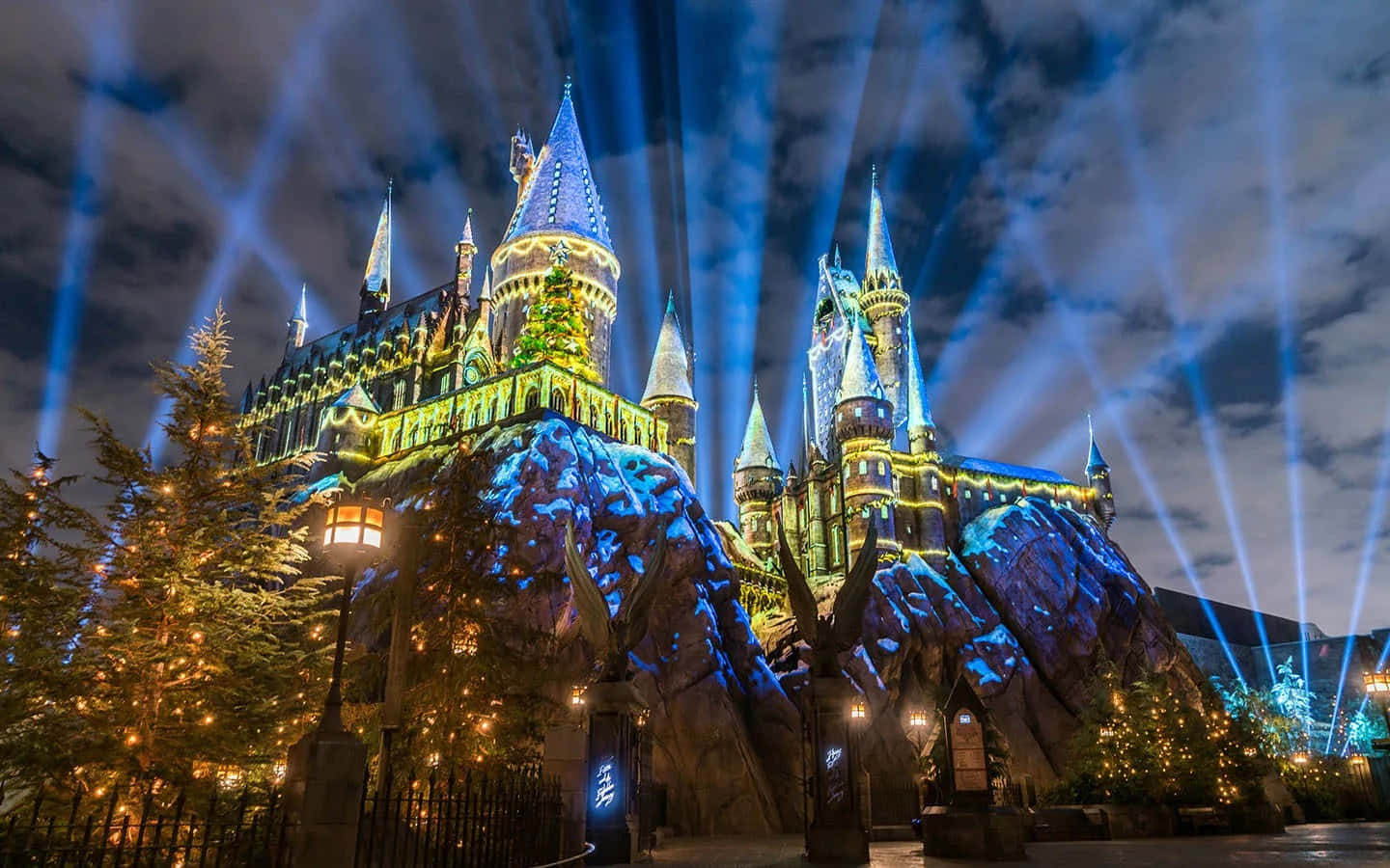 Harry Potter Christmas 桌布 壁紙 — 霍格華茲城堡在夜晚被藍色聚光燈和周圍樹木的節日燈光照亮。