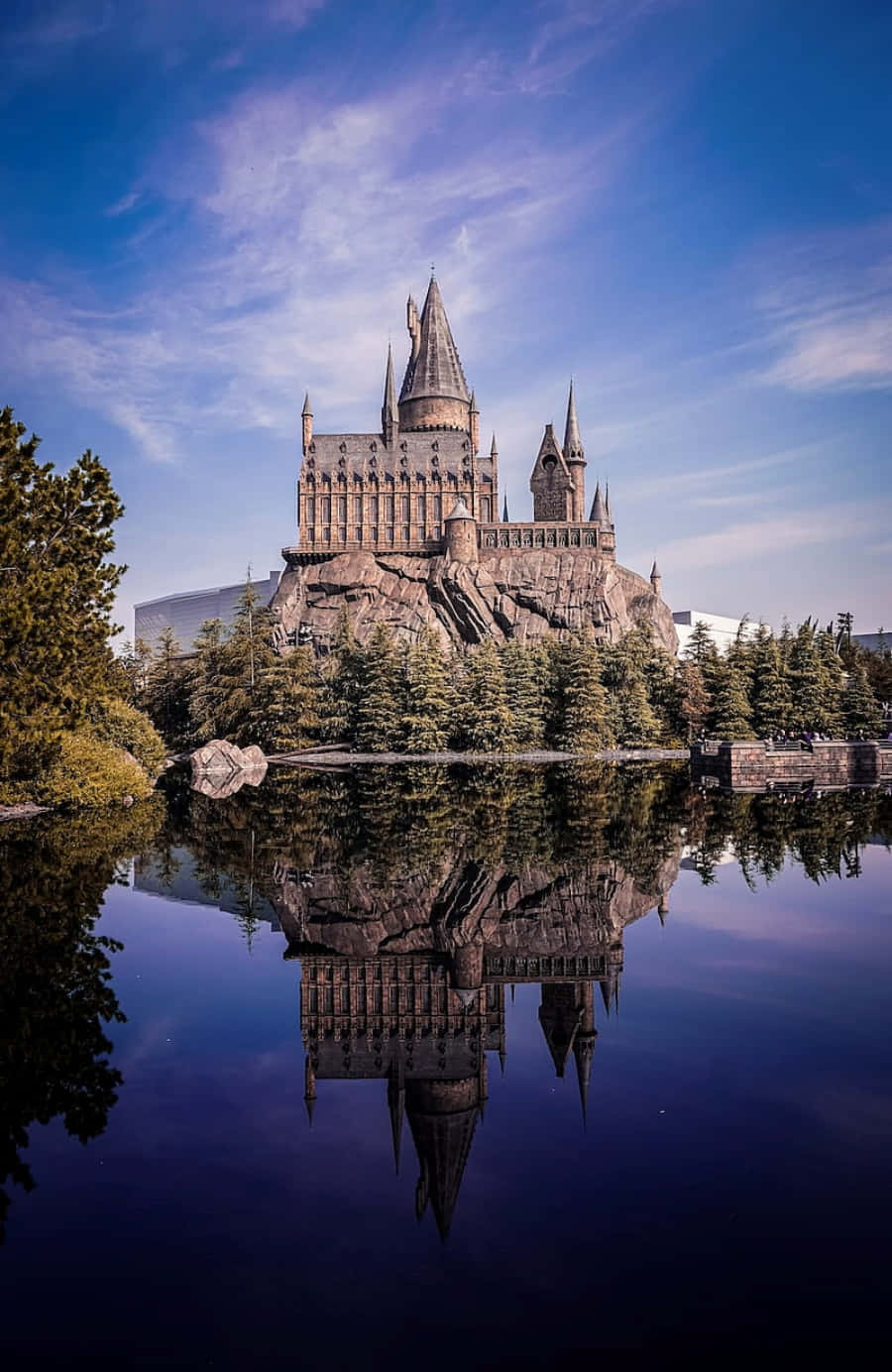 The Hogwarts Lake 桌布 壁紙 — 霍格華茲城堡從岩石懸崖上雄偉地聳立，完美地倒映在平靜的水面上，在充滿活力的藍天下。