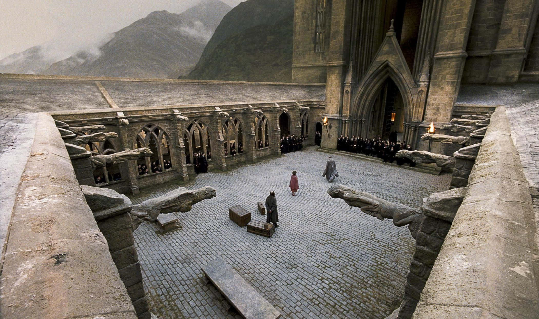 The Battle Of Hogwarts 桌布 壁紙 — 霍格華茲庭院的高角度視圖，有石像鬼和學生在陰天下的鵝卵石上行走。