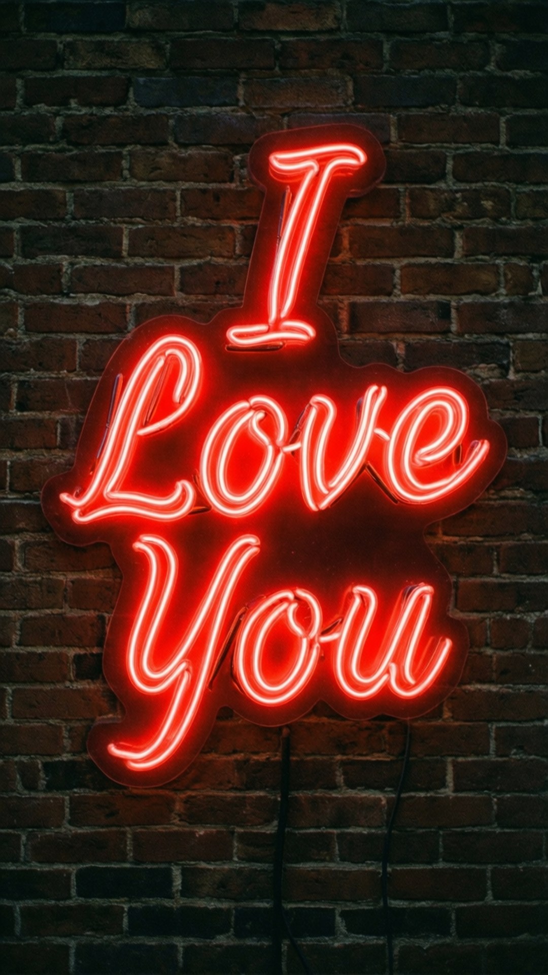 霓虹愛心標誌 壁紙 — 一個發光的紅色霓虹燈牌，上面寫著「I Love You」，在夜晚的深色磚牆上投射出溫暖的光芒。
