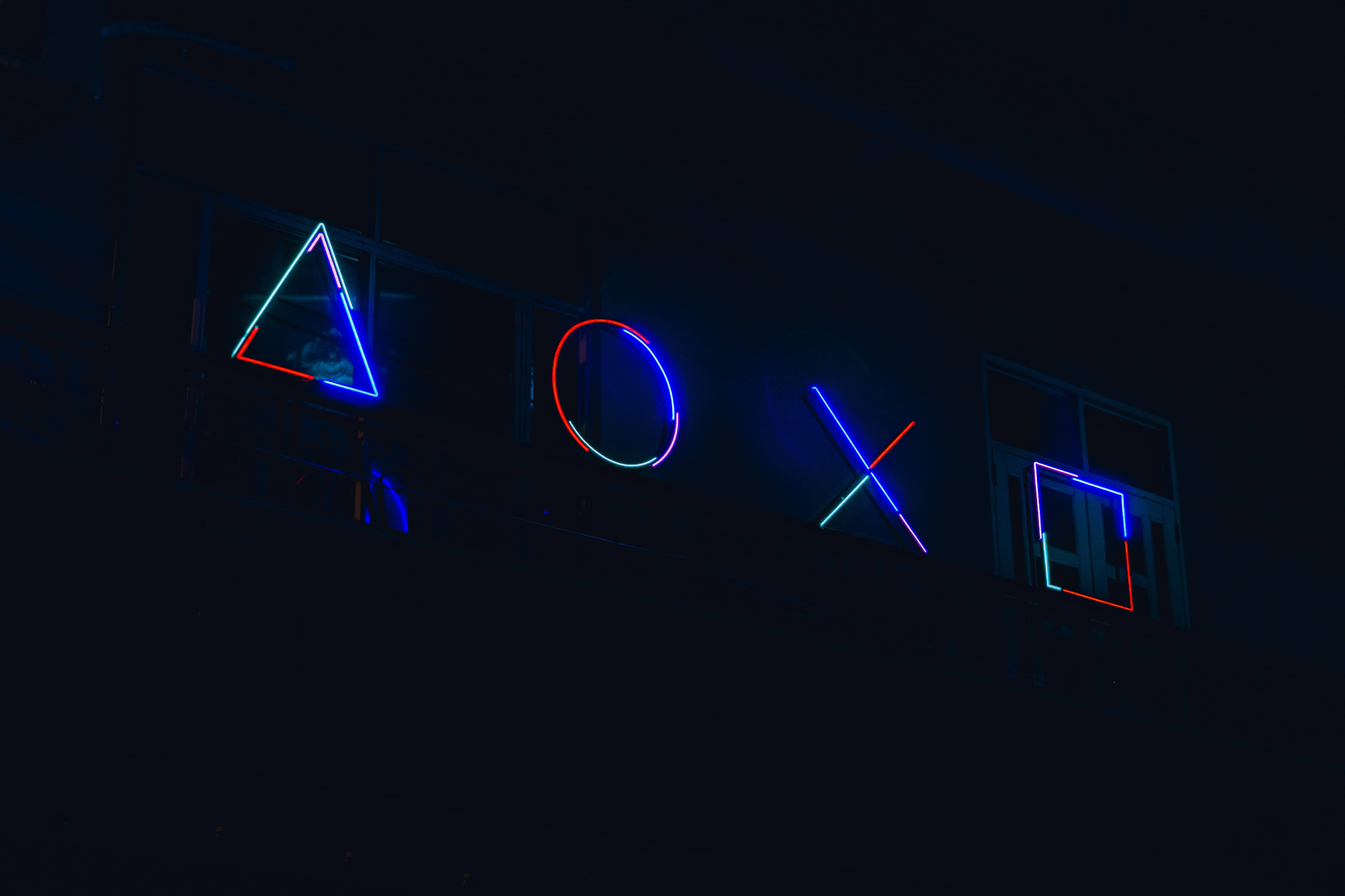 十字架 桌布 壁紙 — 霓虹燈PlayStation控制器符號在黑暗的城市夜景背景下發出鮮豔的藍色和紅色光芒。