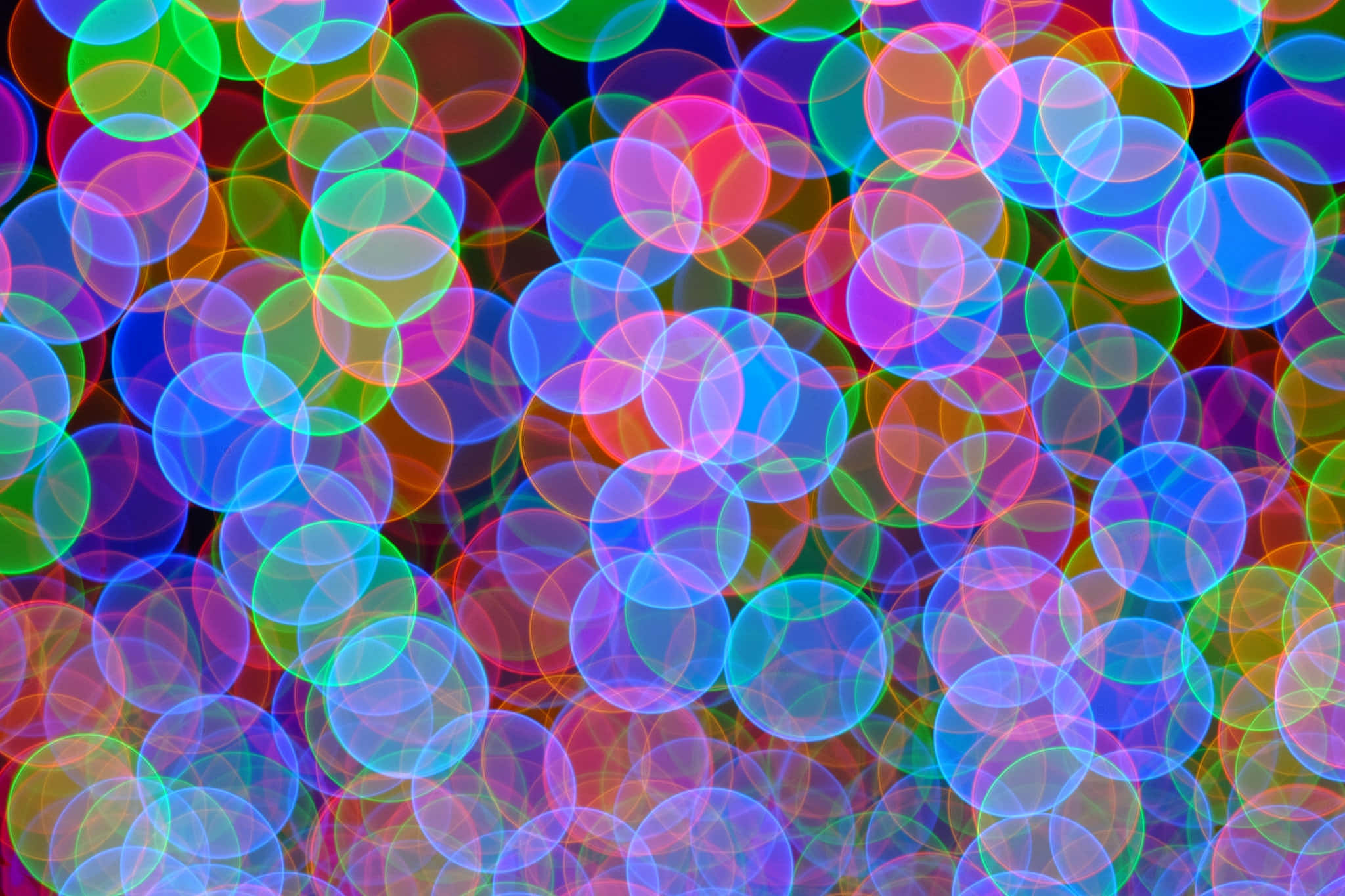 Bokeh 桌布 壁紙 — 霓虹色調中充滿活力的重疊光環在深色背景上創造出令人眼花繚亂的抽象散景圖案。