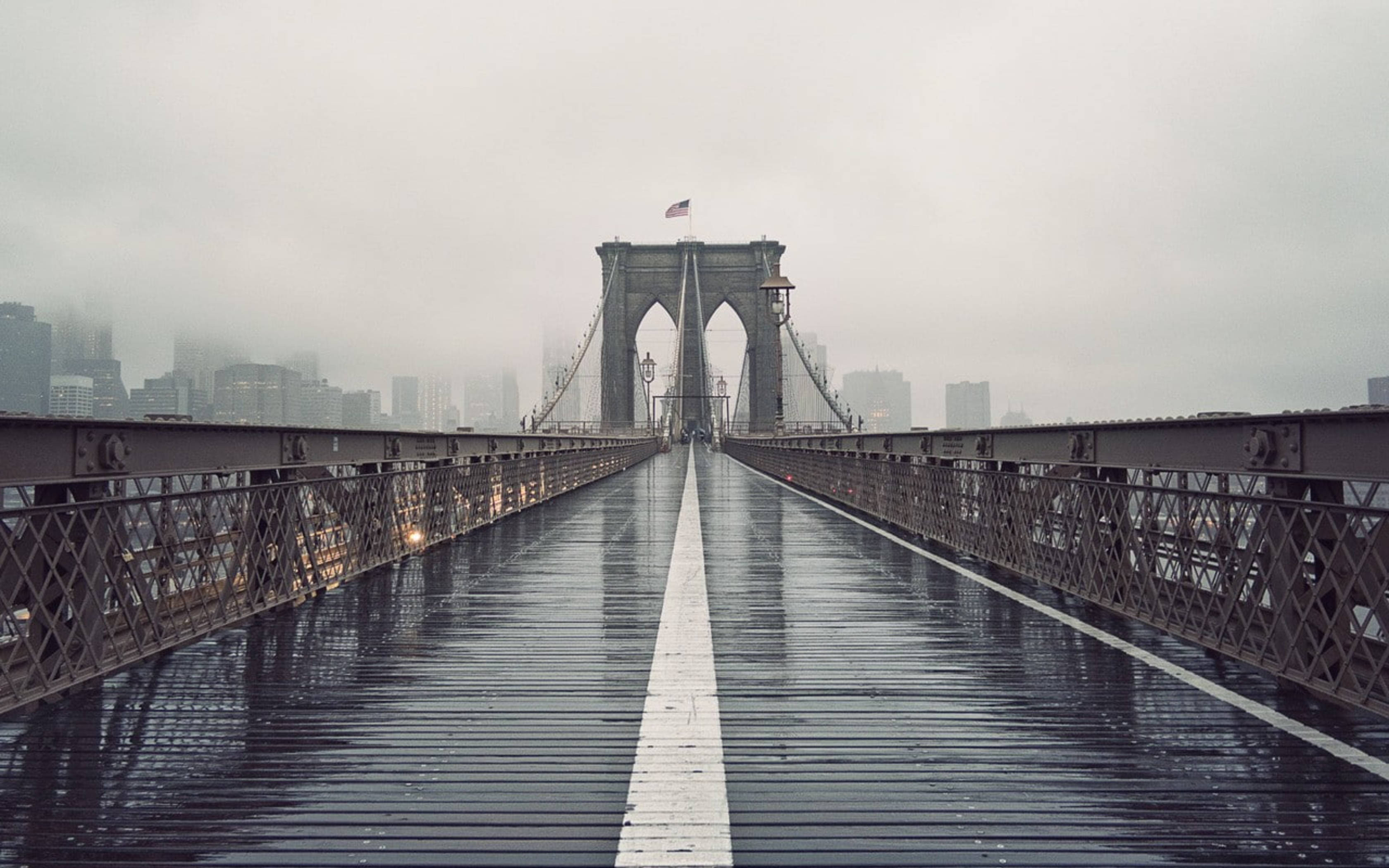 Rainy Day 桌布 壁紙 — 霧中的布魯克林大橋，濕漉漉的木板上映照著灰色的天空和遠處被霧氣籠罩的城市建築。
