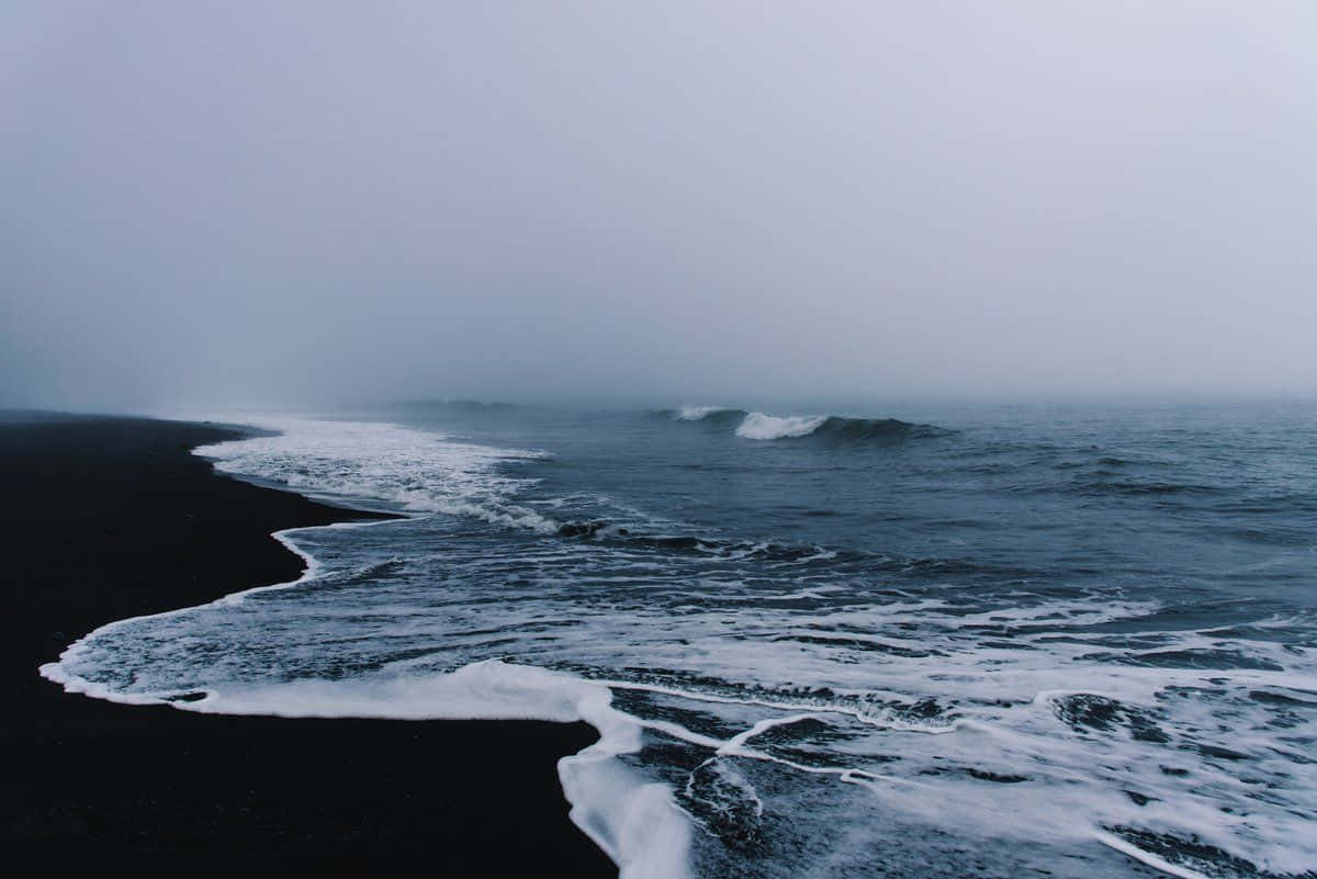 海灘 桌布 壁紙 — 霧氣朦朧的海浪拍打著黑色火山沙灘，天空灰暗多雲。