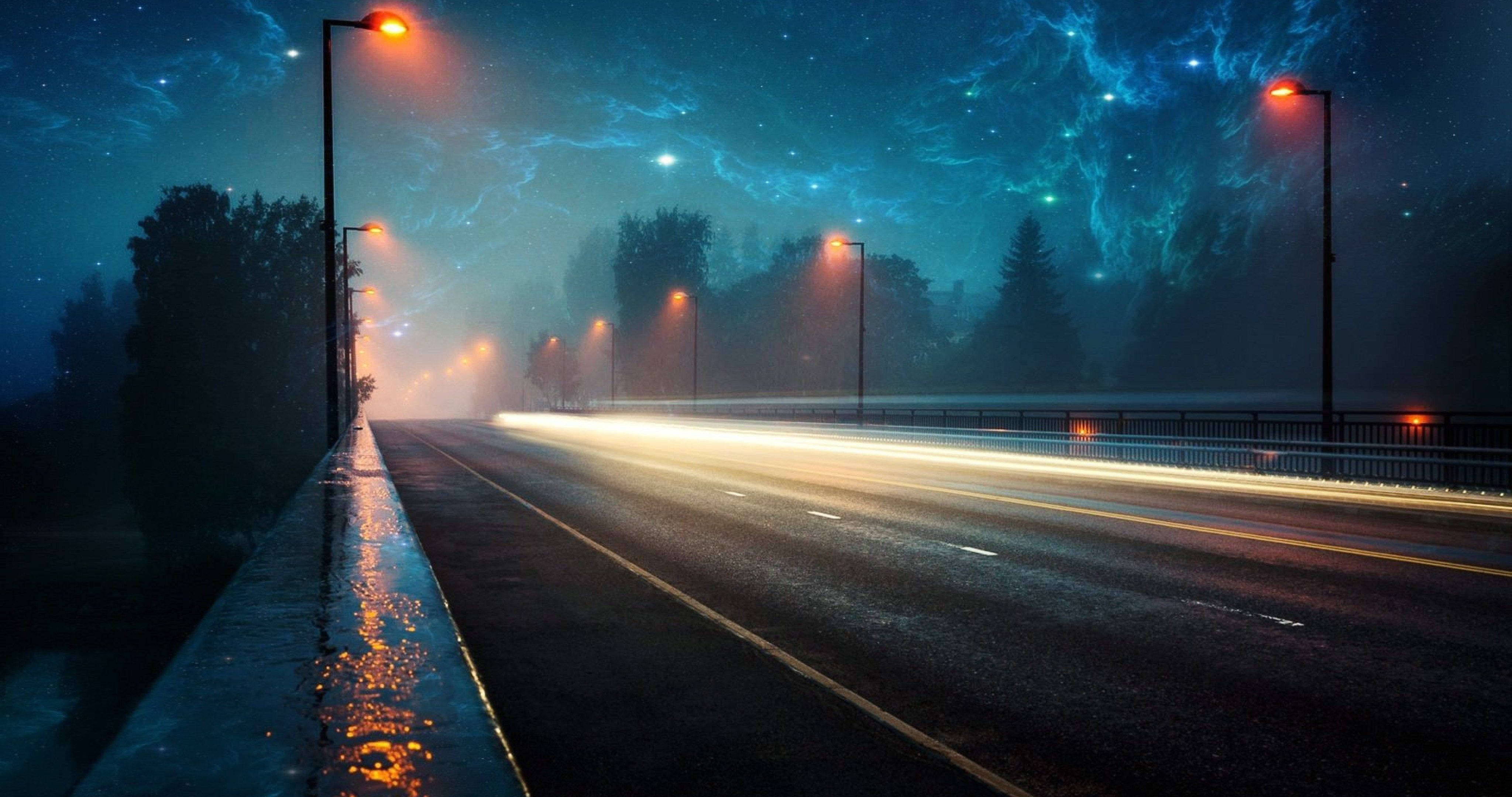 美學 桌布 壁紙 — 霧氣瀰漫的夜晚道路，在發光路燈下，有汽車燈光的條紋和星光閃爍的電藍色天空。