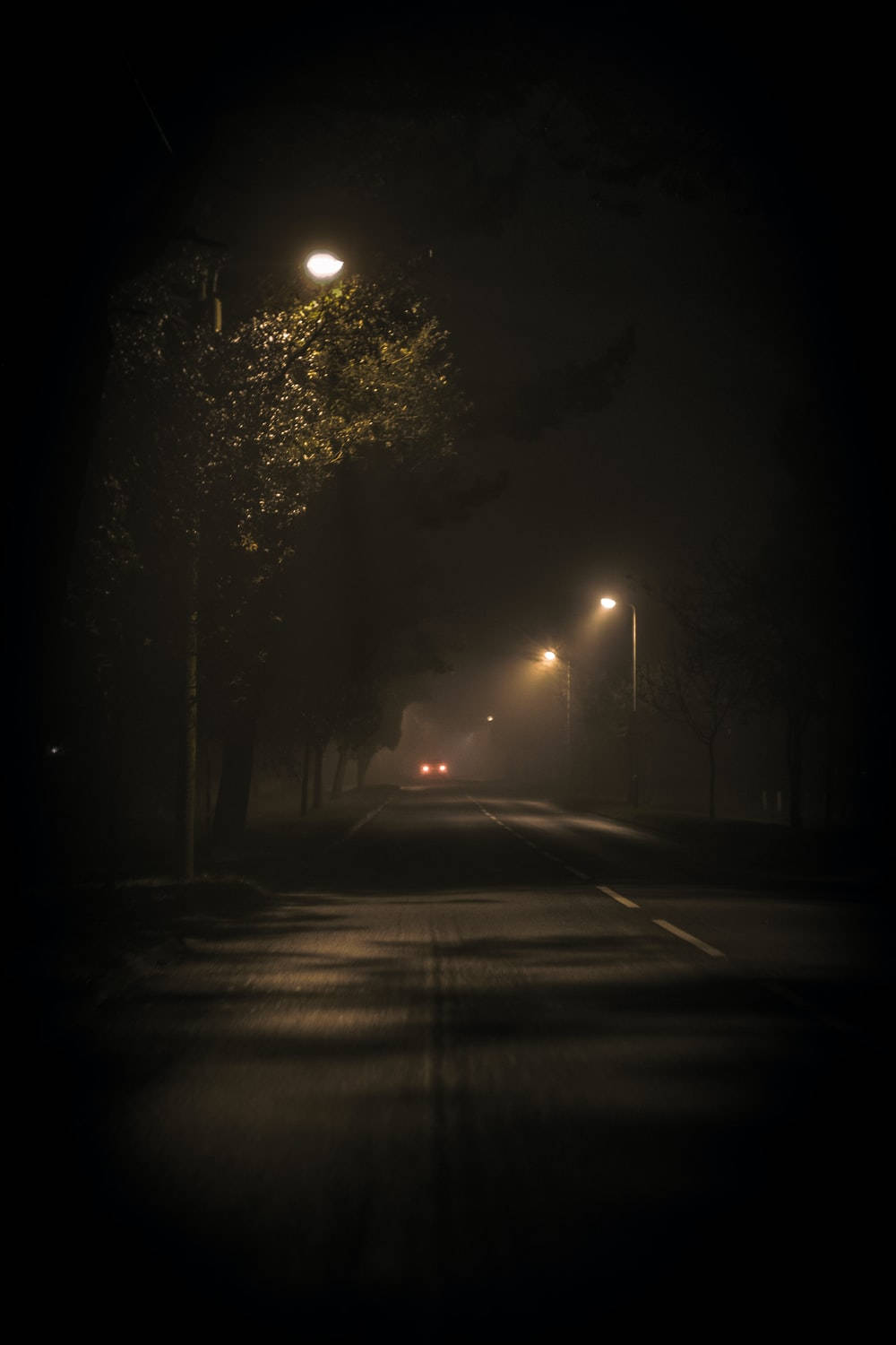 黑夜 桌布 壁紙 — 霧氣瀰漫的夜晚道路，由街燈照亮，遠處汽車的車頭燈穿過霧氣。
