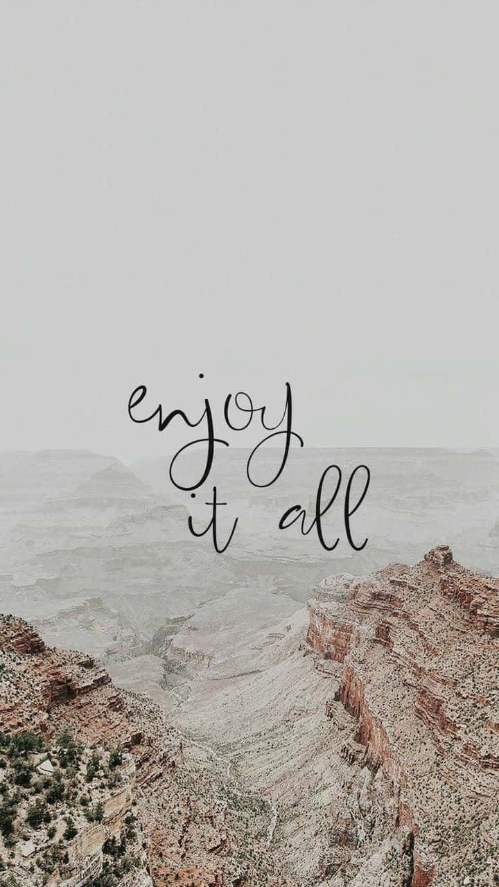 Positivity Aesthetic 桌布 壁紙 — 霧氣瀰漫的峽谷景色，層層疊疊的岩石結構，以及優雅草書寫成的「enjoy it all」字句。