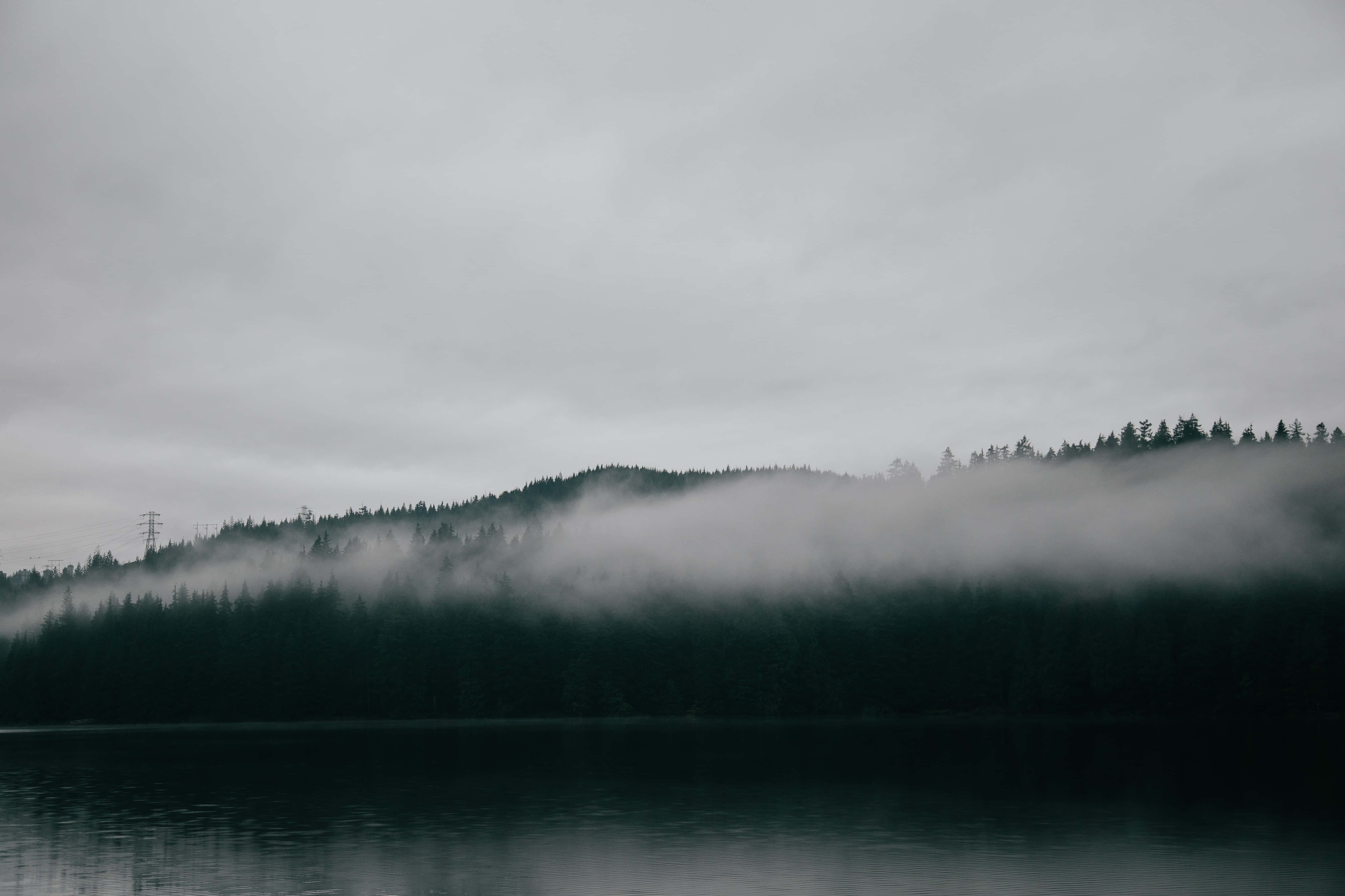 Twitter Header 桌布 壁紙 — 霧氣瀰漫的湖泊倒映著陰沉天空，薄霧籠罩著陰雲下樹木繁茂的山坡。