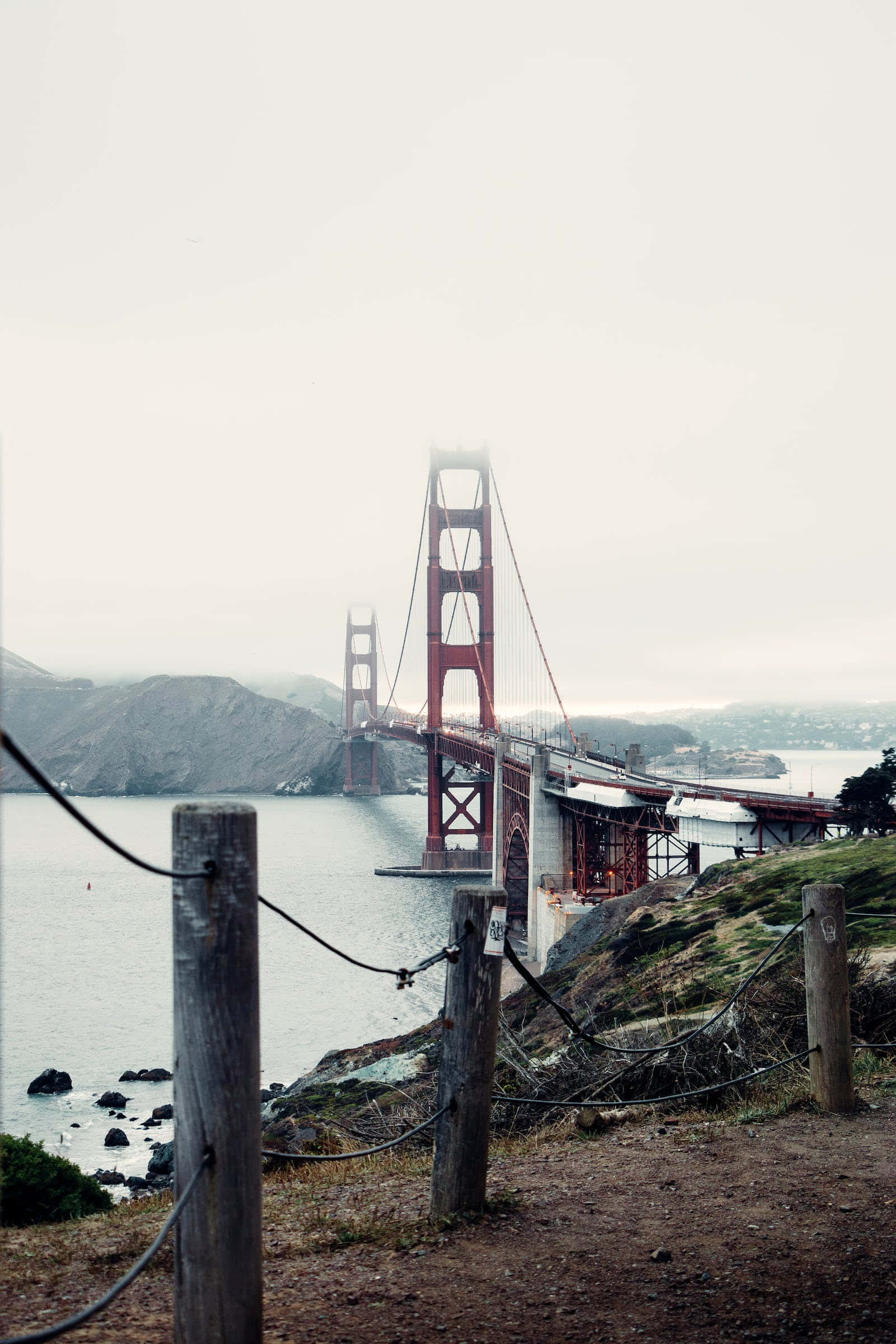San Francisco Fog 桌布 壁紙 — 霧氣籠罩的早晨，金門大橋被木柵欄和岩石海岸線框住。