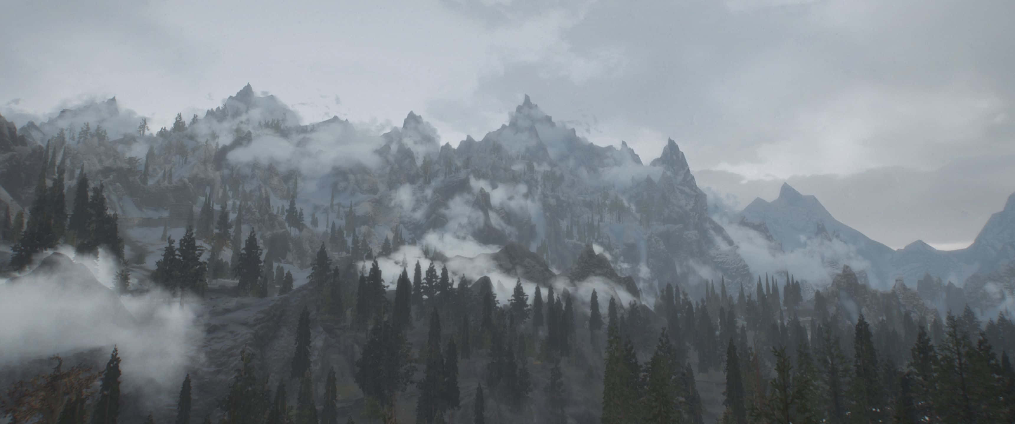 3440x1440p The Elder Scrolls V Skyrim 桌布 壁紙 — 霧氣籠罩的灰色山脈在陰天中升起於茂密森林之上，霧氣依附在山峰和樹木上。