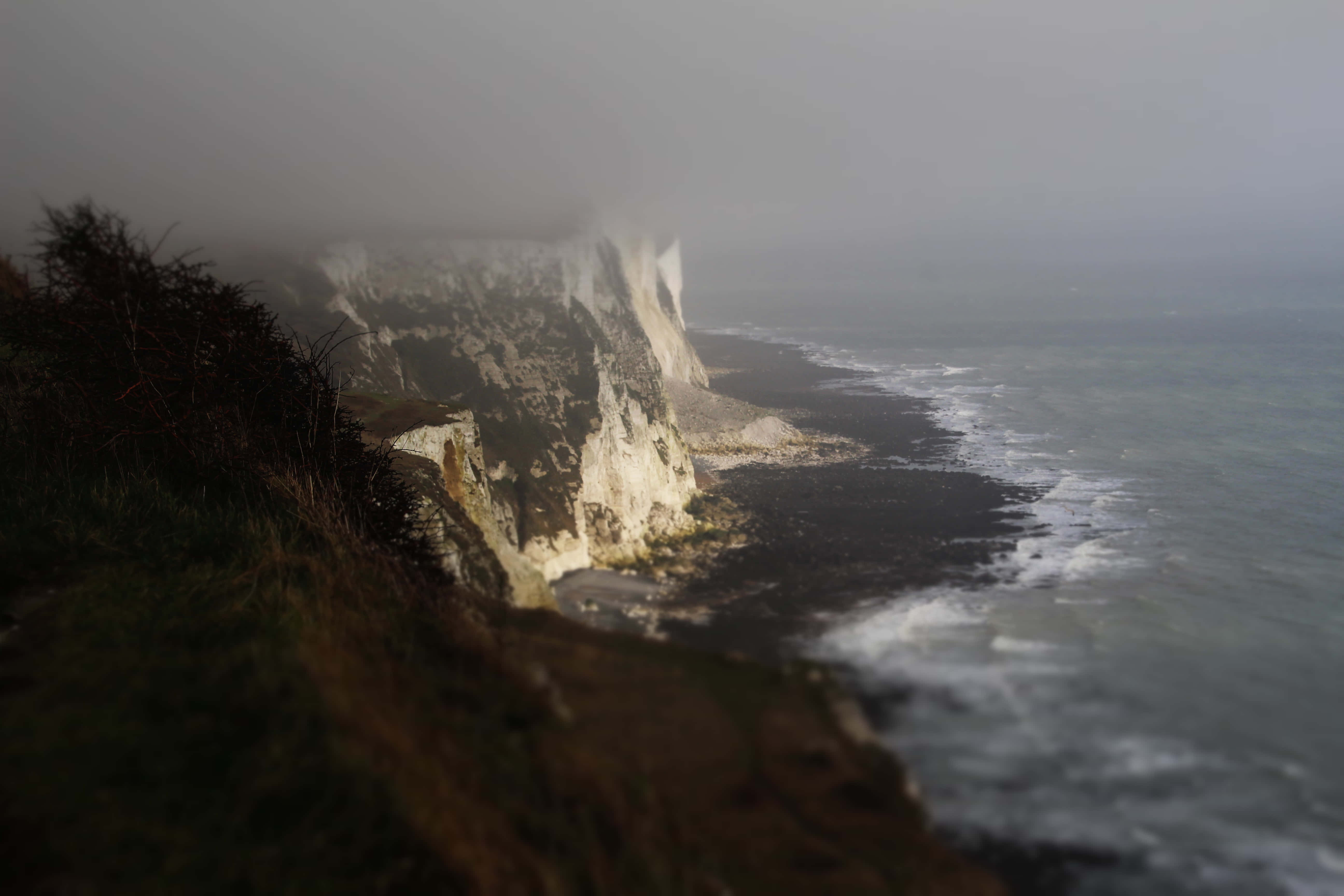 England 桌布 壁紙 — 霧氣籠罩的白色岩石海岸懸崖，在陰天之下與翻騰的灰色大海相遇。