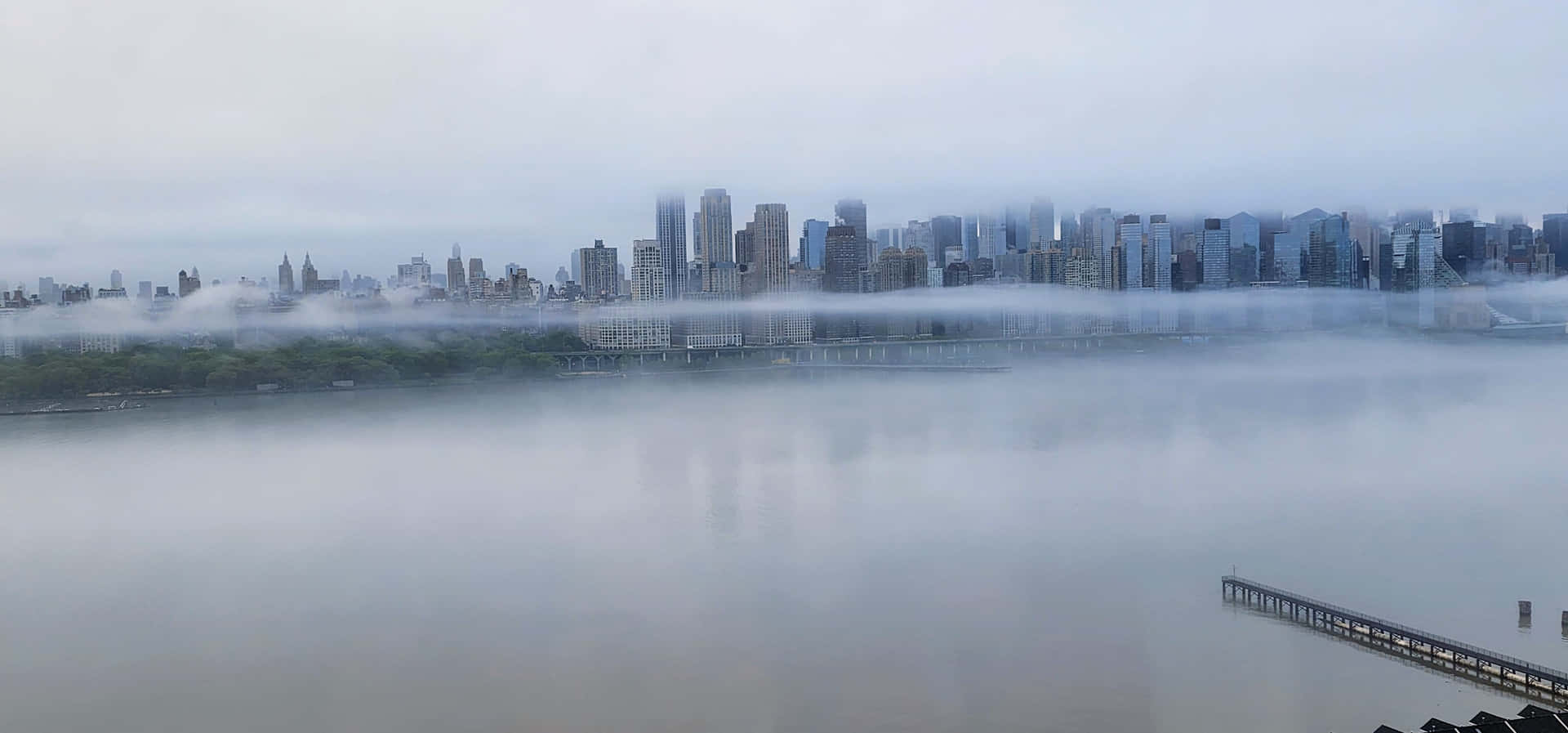 New York City Foggy Skyline 壁紙 — 霧氣籠罩的黎明覆蓋著廣闊的城市景觀，摩天大樓從平靜河流上的霧氣中浮現。
