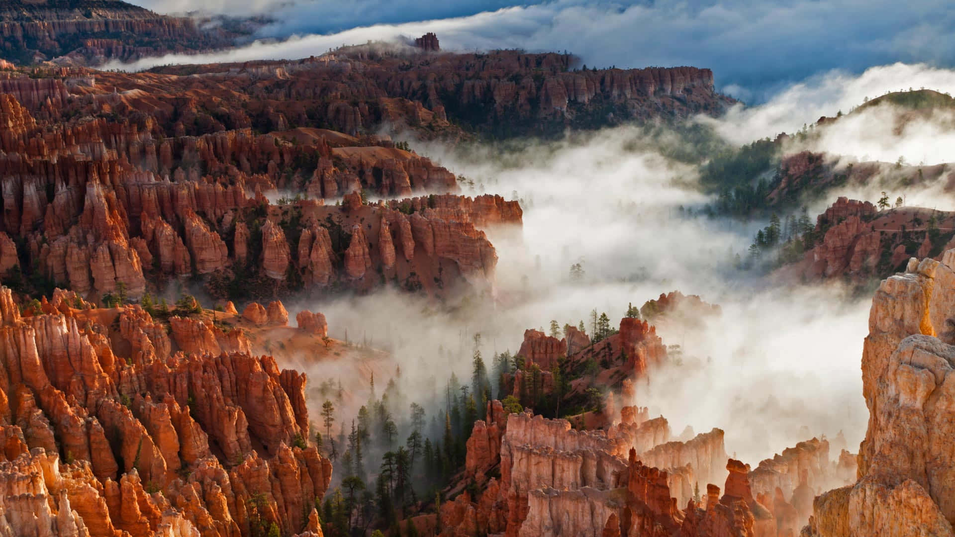 Utah 桌布 壁紙 — 霧氣雲霧飄過高聳的橙色岩柱，在日出時分的戲劇性峽谷景觀中。