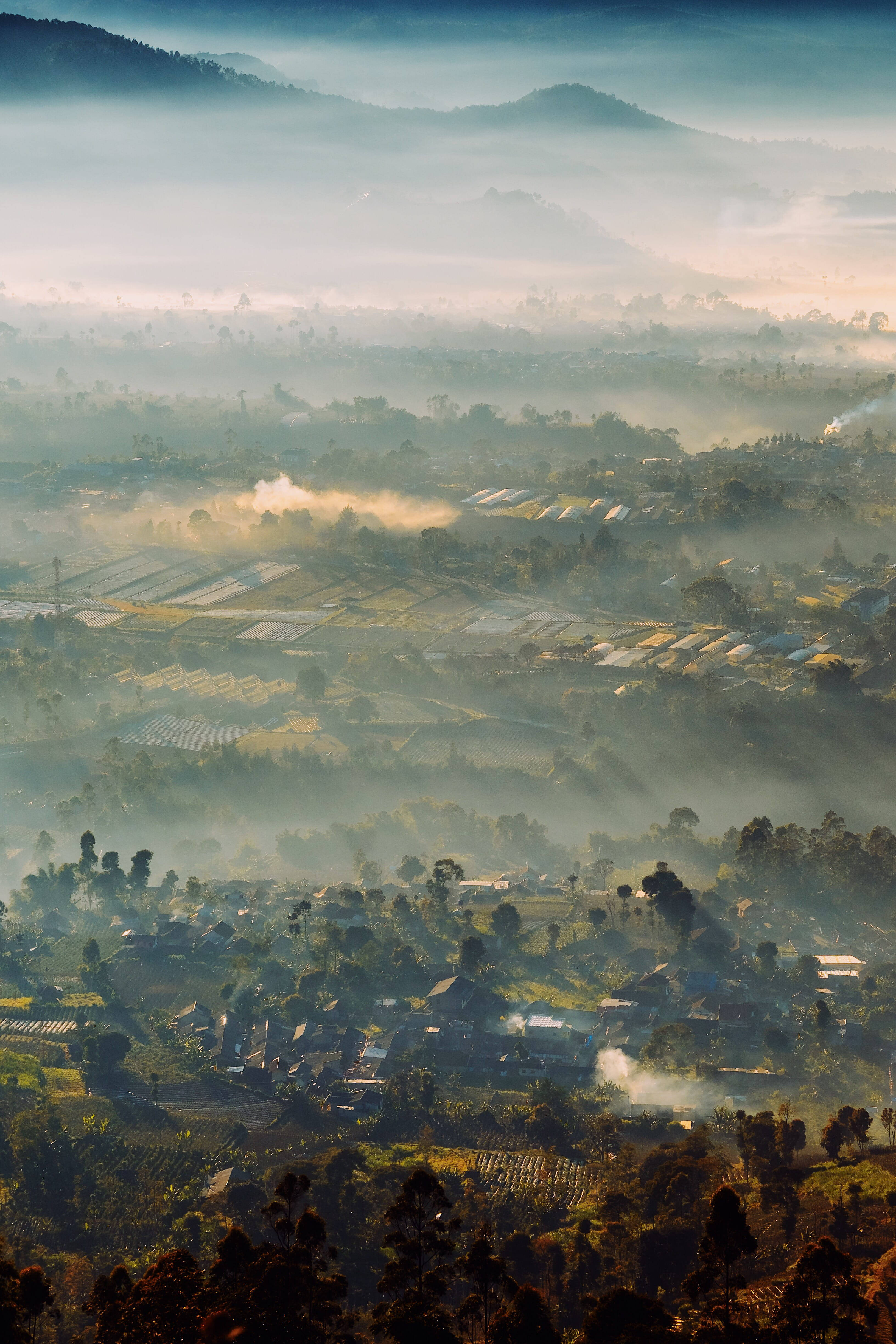 bandung 桌布 壁紙 — 霧濛濛的黎明籠罩著一個山谷，山谷中有梯田農場和散落在起伏山丘間的村莊房屋。