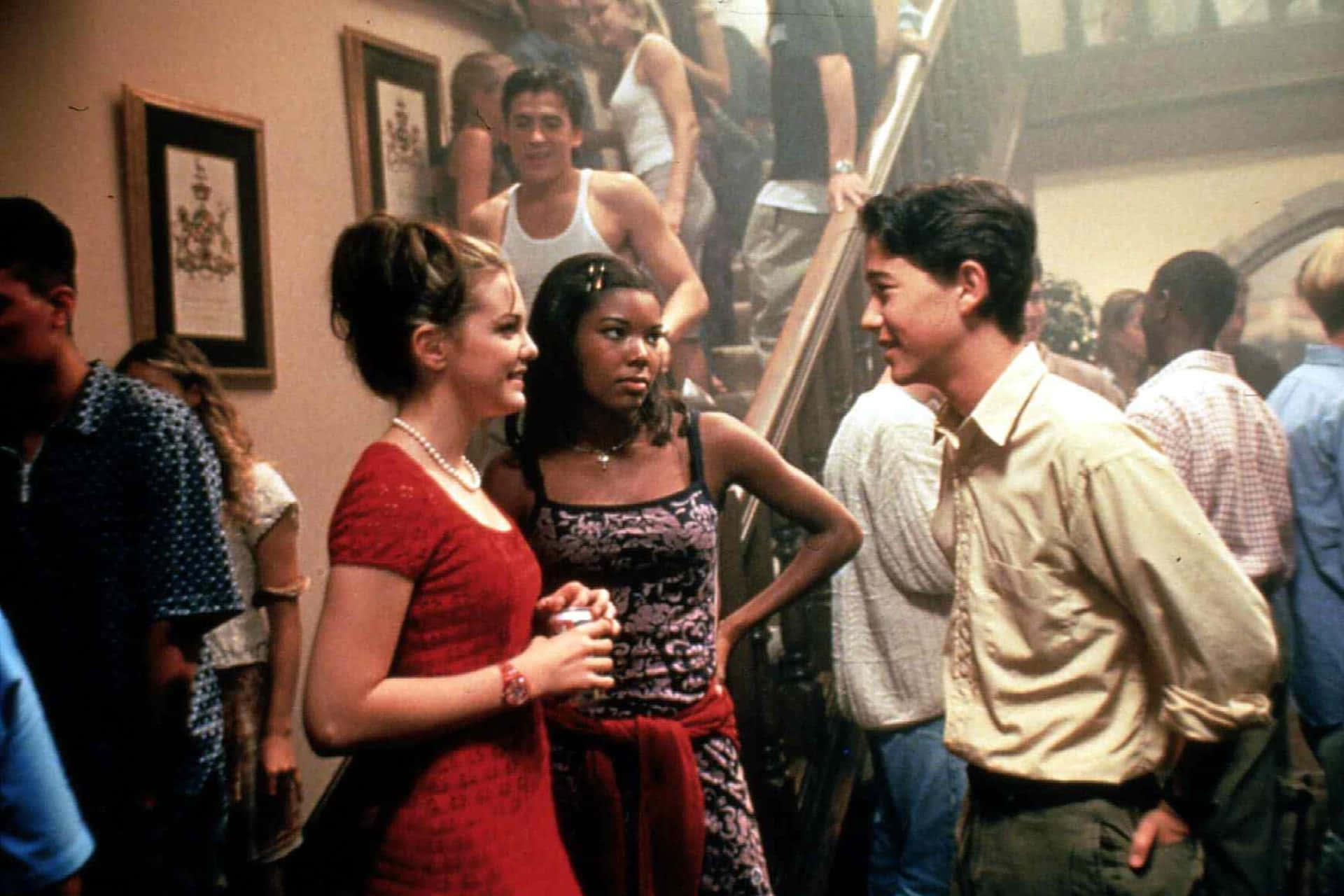 House Party 桌布 壁紙 — 青少年在擁擠的室內派對中交流，現場有溫暖的燈光和牆上掛著的裱框藝術品。