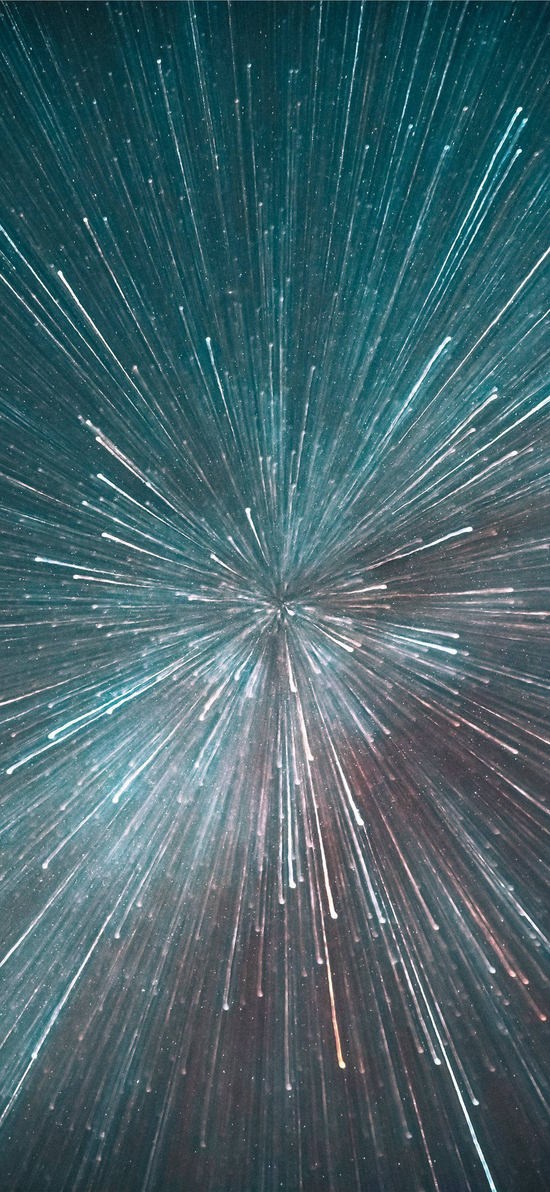 美學 iPhone 壁紙 桌布 壁紙 — 青綠色和銀色光芒的輻射狀星塵條紋從中心點爆發，背景是宇宙般的黑暗。