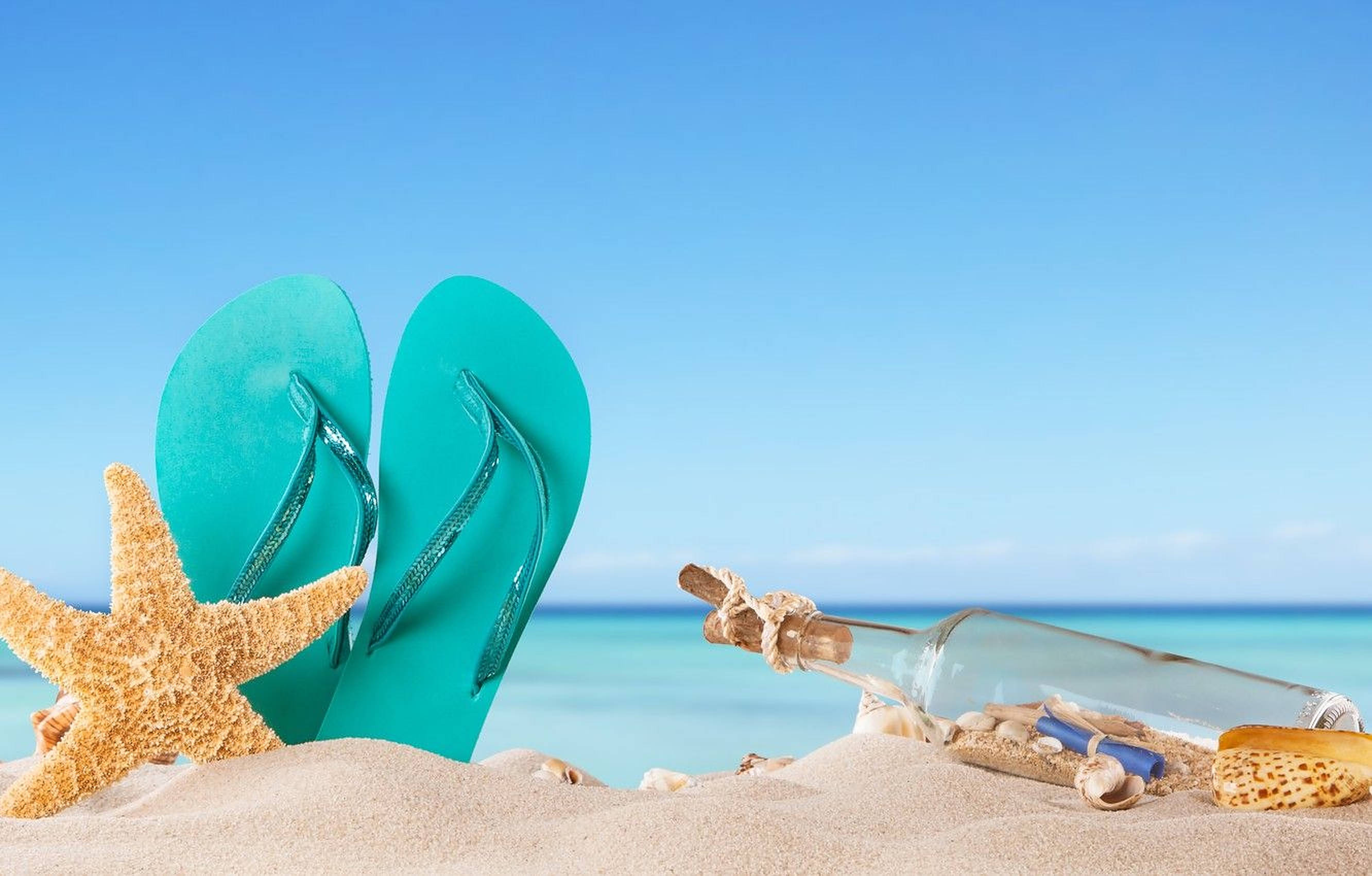 Beach Vacation 桌布 壁紙 — 青綠色的夾腳拖鞋放在沙灘上，旁邊有海星和一個裝有訊息的瓶子，在陽光明媚的海灘上。