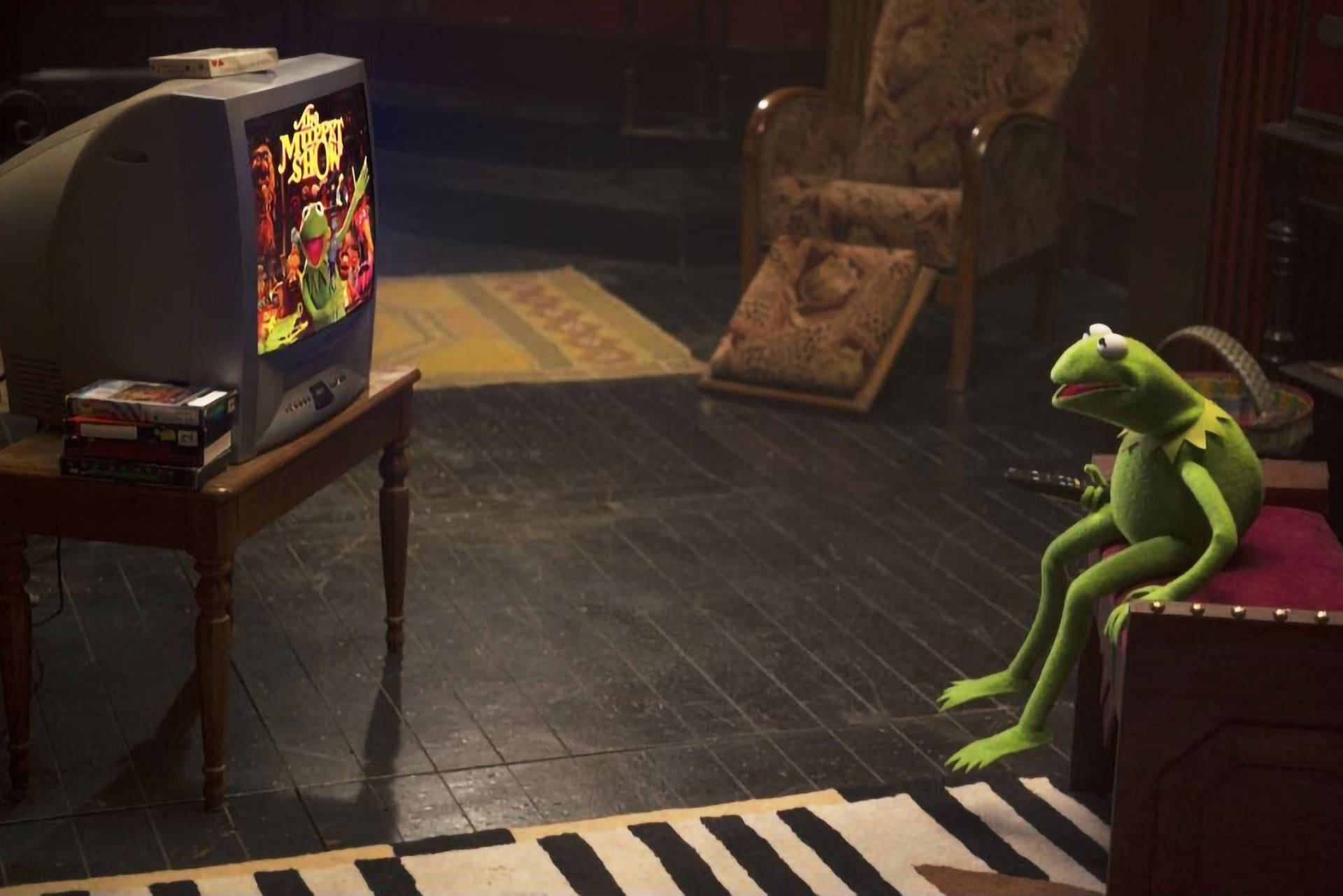 muppets 桌布 壁紙 — 青蛙Kermit坐在行李箱上，在昏暗的復古客廳裡看著復古電視上的《布偶秀》。