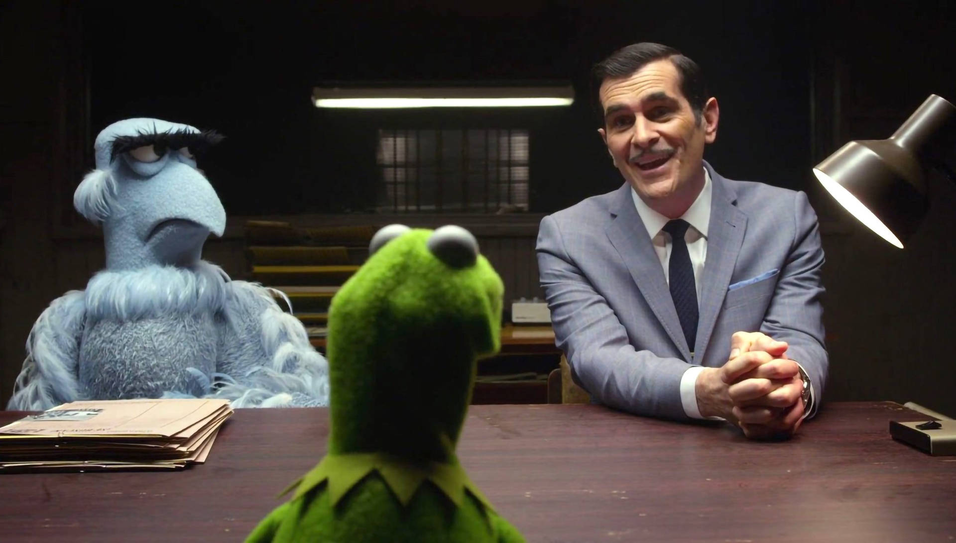 muppets 桌布 壁紙 — 青蛙柯密特坐在一張辦公桌前，面對著一個微笑的西裝男子和一個藍色毛絨木偶，在一個燈光昏暗的辦公室裡。