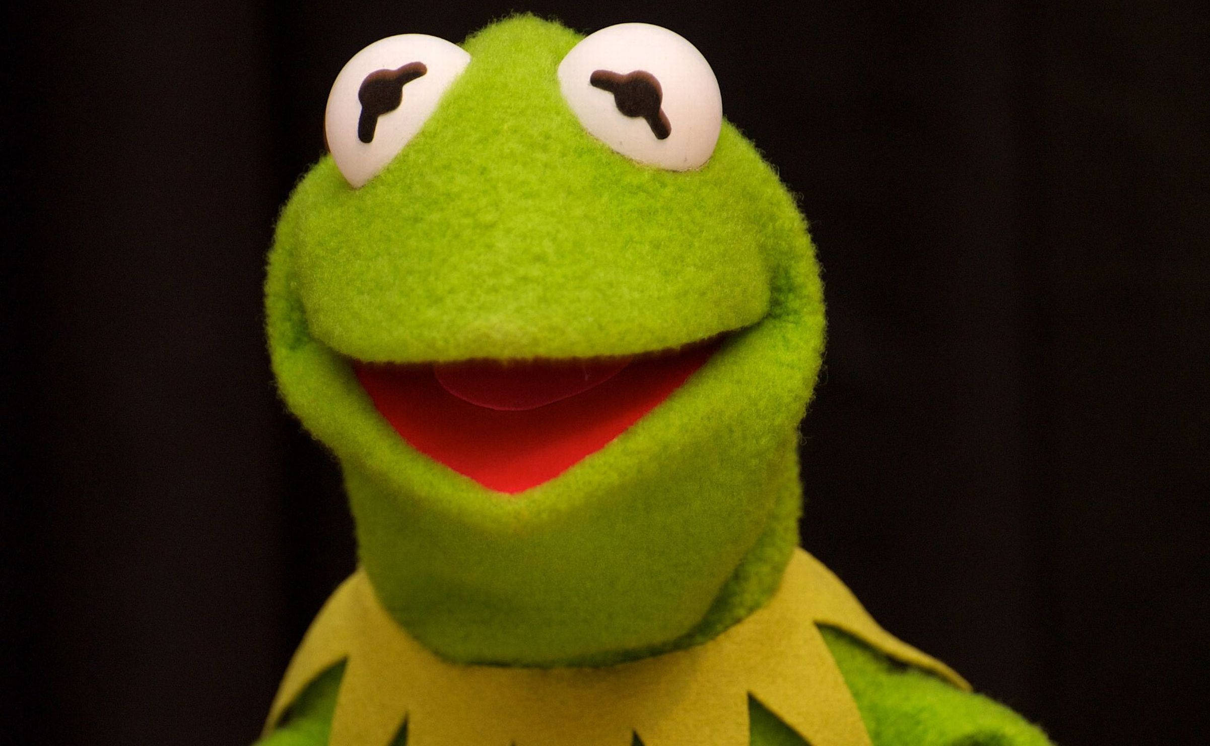 kermit 桌布 壁紙 — 青蛙柯密特布偶的特寫，帶有亮綠色氈質感和寬闊歡樂的笑容，背景為深色。