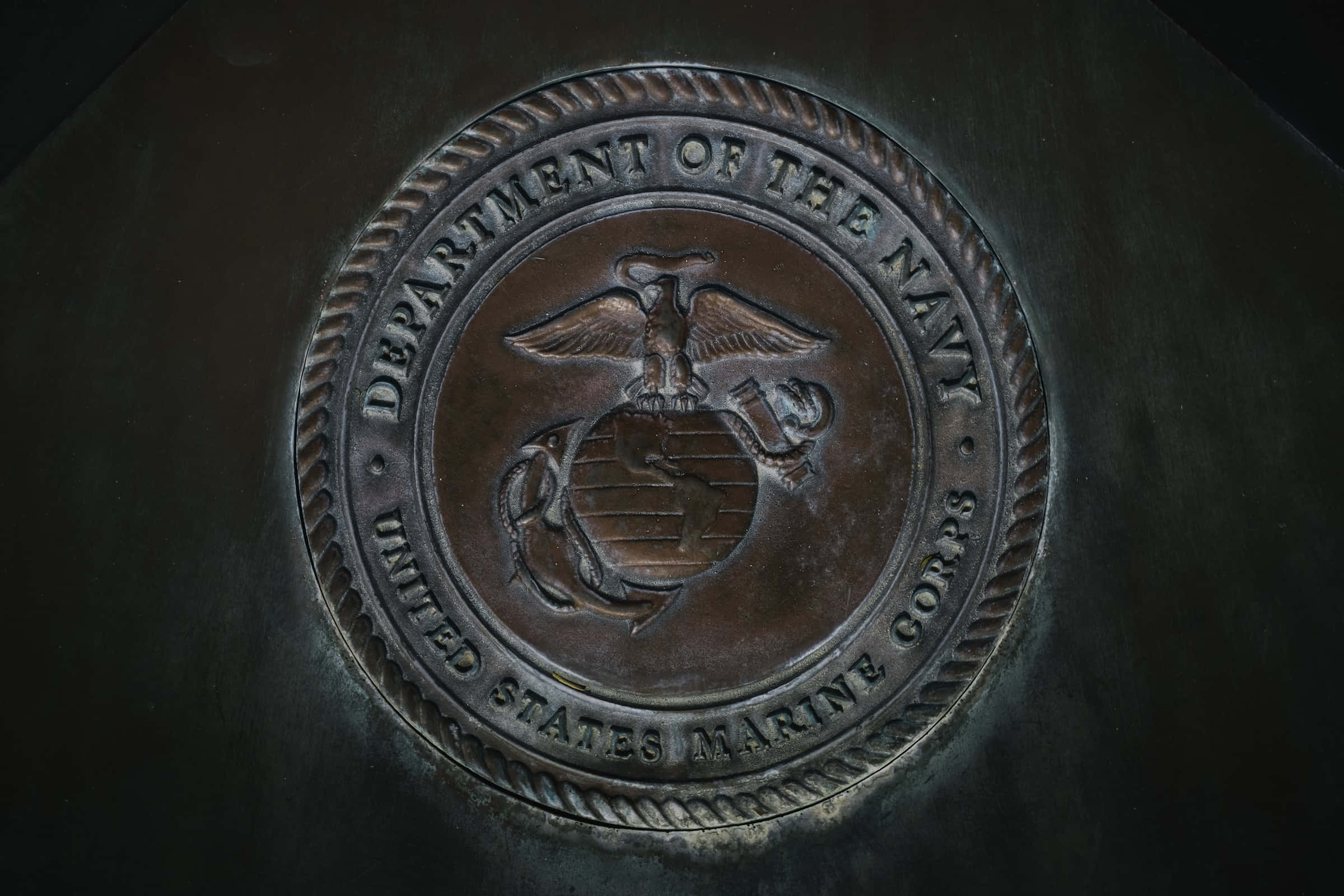 US Marines 桌布 壁紙 — 青銅色美國海軍陸戰隊徽章（鷹、地球、錨）的特寫，置於深色紋理金屬表面上。