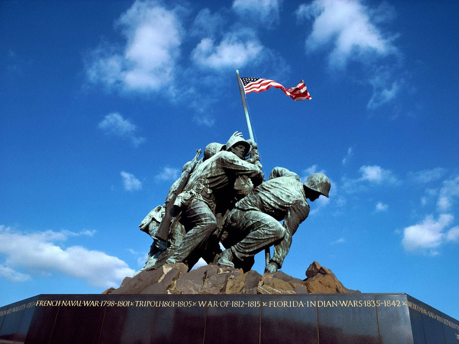 Memorial 桌布 壁紙 — 青銅雕像，士兵在岩石底座上舉起旗幟，背景是明亮的藍天和零星雲朵。