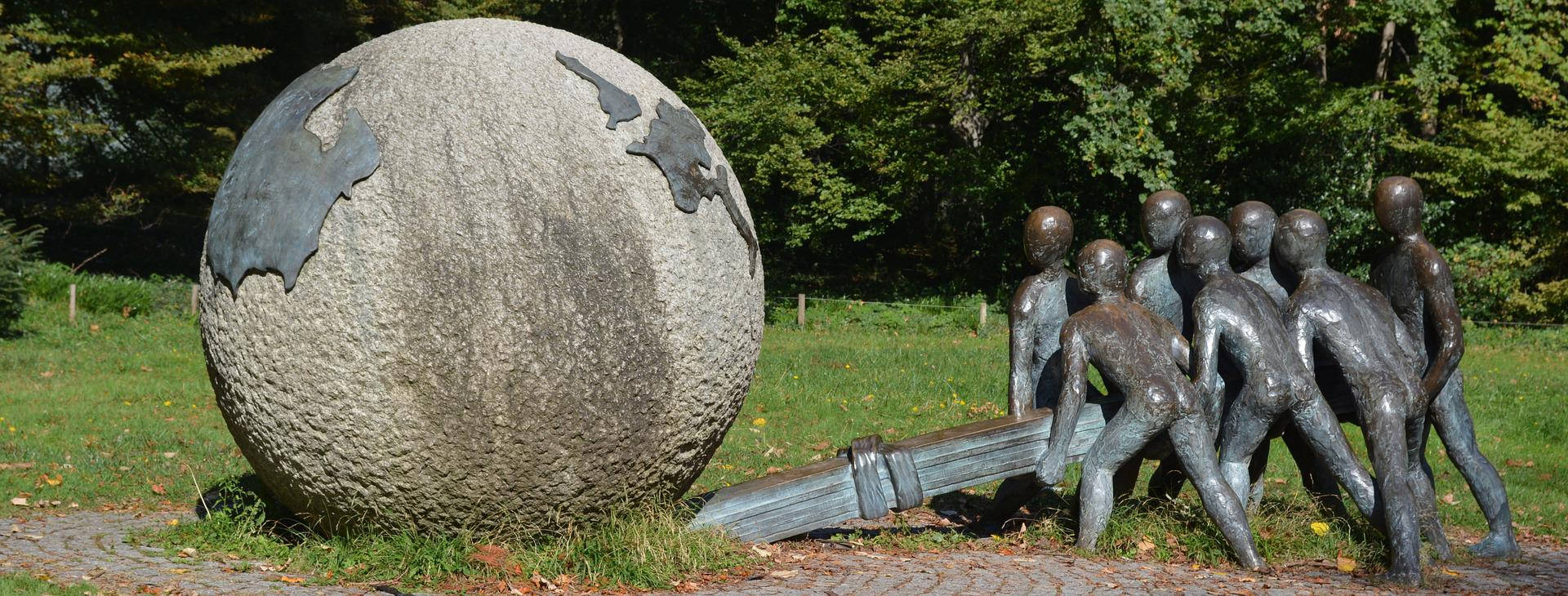 World 桌布 壁紙 — 青銅雕像，描繪孩子們在陽光明媚、綠樹成蔭的公園中推動一個大型紋理地球儀雕塑。