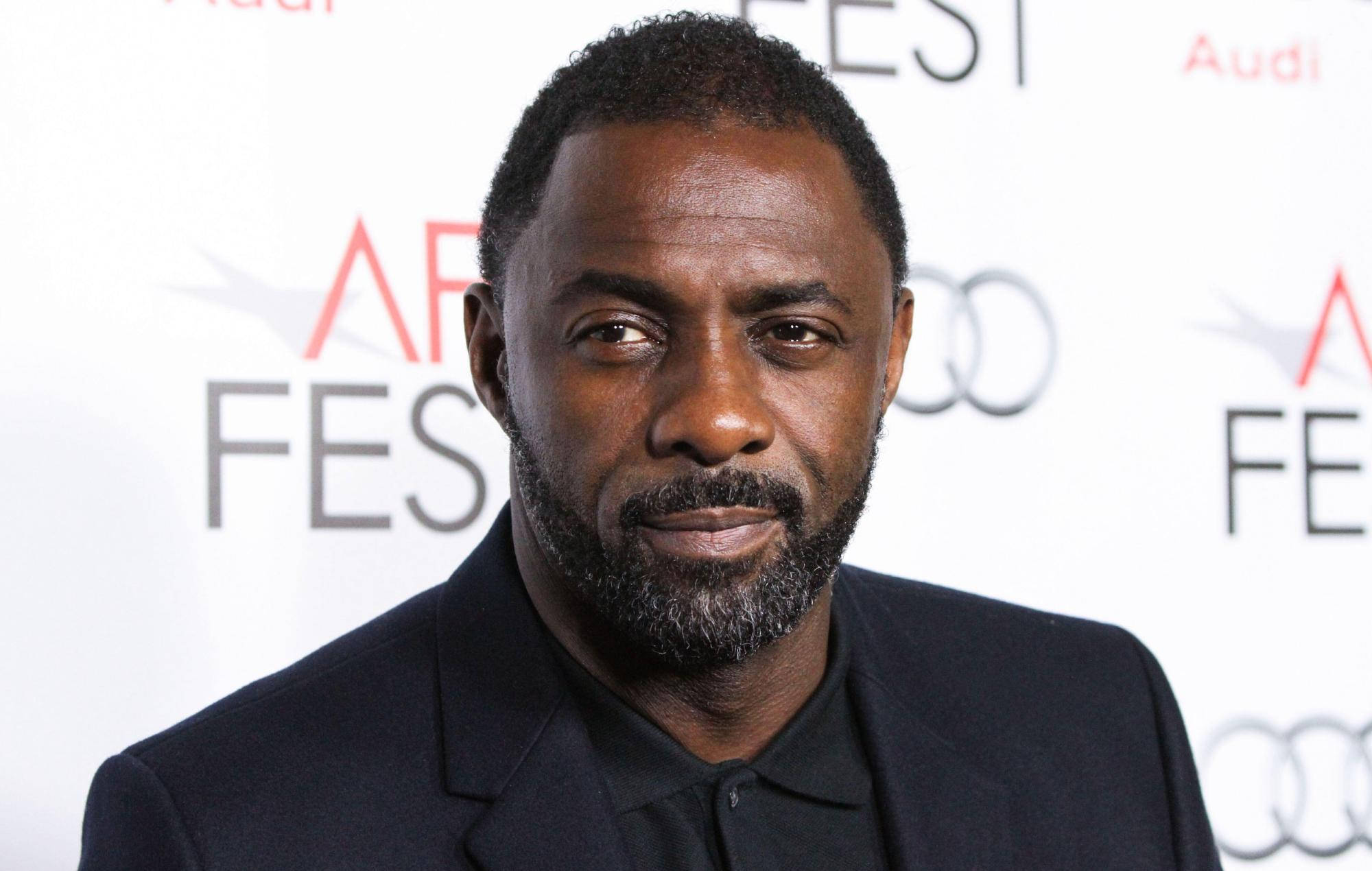idris elba 桌布 壁紙 — 非裔美國男子留鬍鬚，身穿黑色西裝，身後有「AFI FEST」和「Audi」標誌的活動。