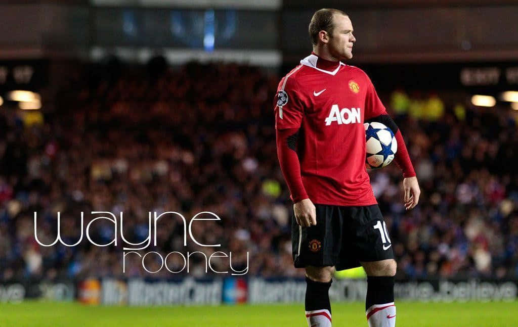 Wayne Rooney 桌布 壁紙 — 韋恩·魯尼身穿紅色曼聯球衣，在燈光璀璨的球場上抱著足球，身後是模糊的人群。