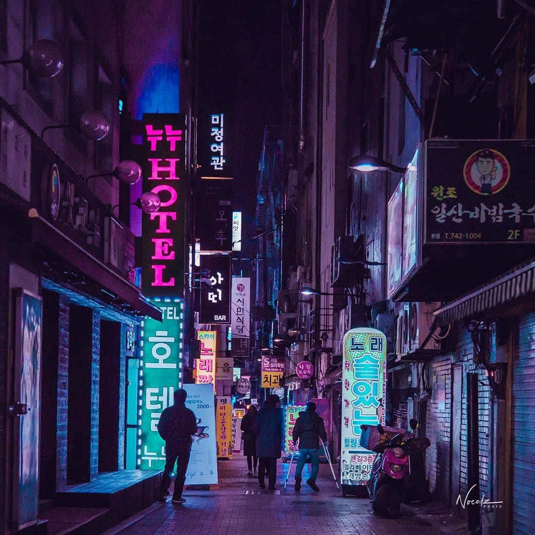 暗黑風格 桌布 壁紙 — 韓國城市夜晚一條狹窄的霓虹燈小巷，有發光的招牌和行人走在彩色燈光下。