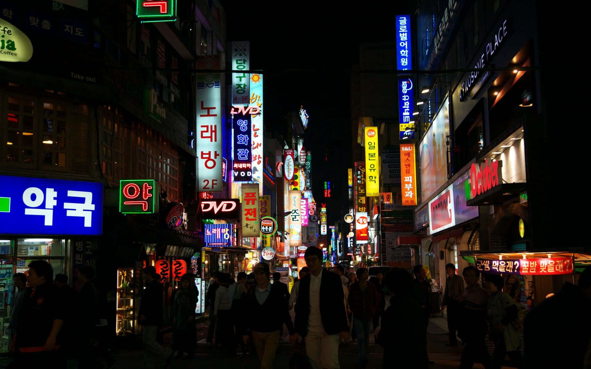 韓國 桌布 壁紙 — 韓國城市夜晚一條繁忙的霓虹燈街道，擠滿行人，閃爍著多語言的招牌。