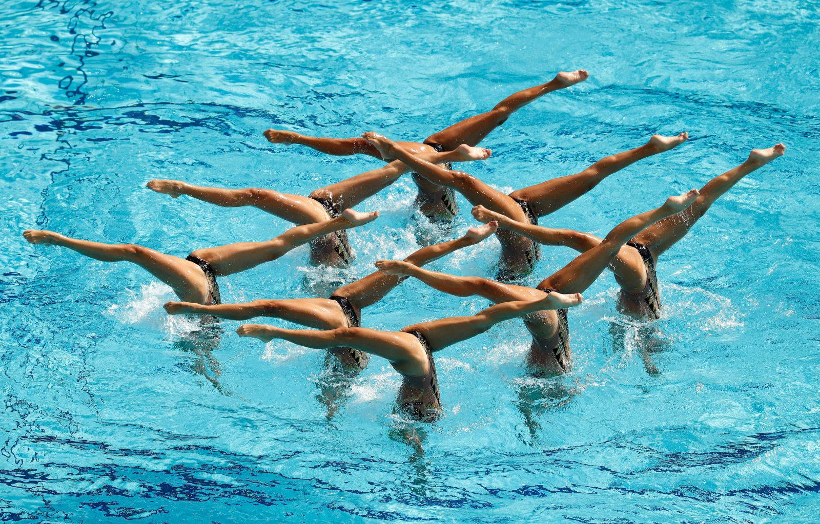 Swimming 桌布 壁紙 — 韻律泳運動員在充滿活力的藍色泳池水中精準地執行高舉過頭的姿勢，產生動態水花。