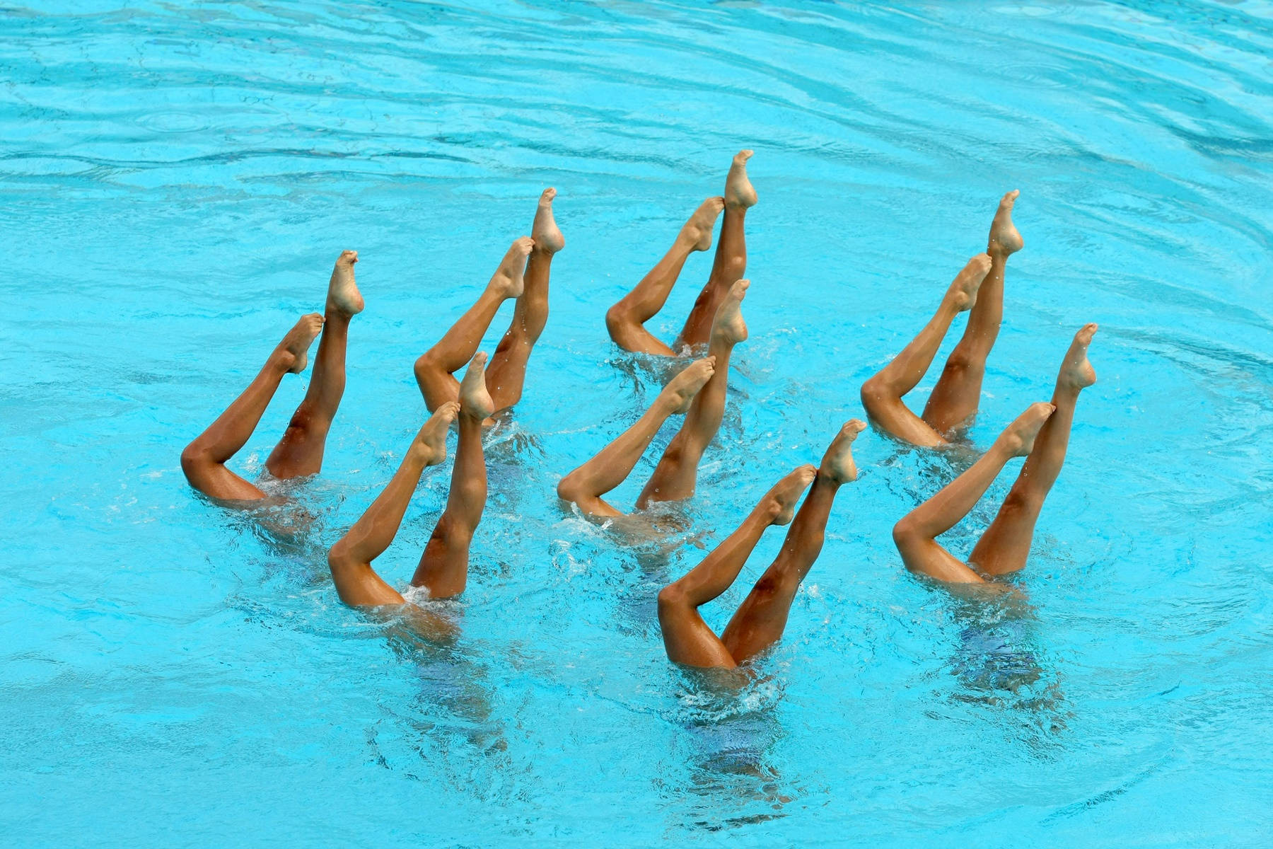 Swimming 桌布 壁紙 — 韻律泳選手在清澈的藍色水面上整齊劃一地舉起雙腿，營造出動感而精準的水上表演。