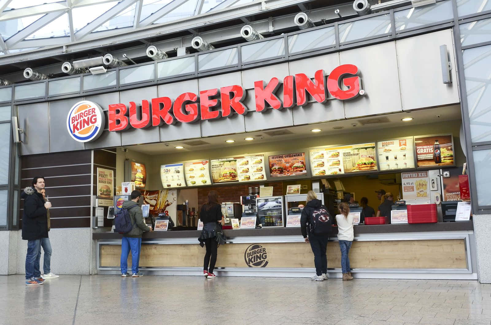Burger King 桌布 壁紙 — 顧客在現代室內環境中，於明亮的紅色招牌下的漢堡王速食櫃檯前排隊。