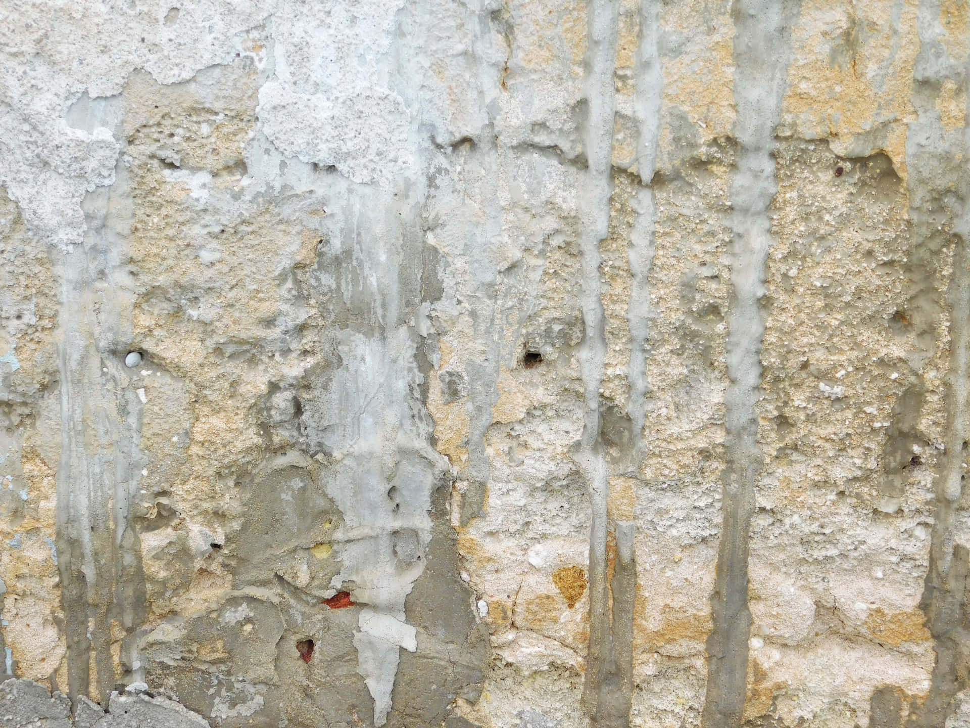 Stone texture 壁紙 — 風化混凝土牆的特寫，灰色灰泥剝落，露出下方黃色石頭，呈垂直條紋。