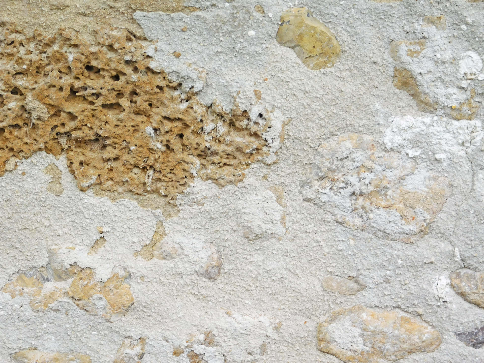 Stone texture 壁紙 — 風化灰泥的特寫，露出下方粗糙紋理的石頭，呈現米色和灰色調。