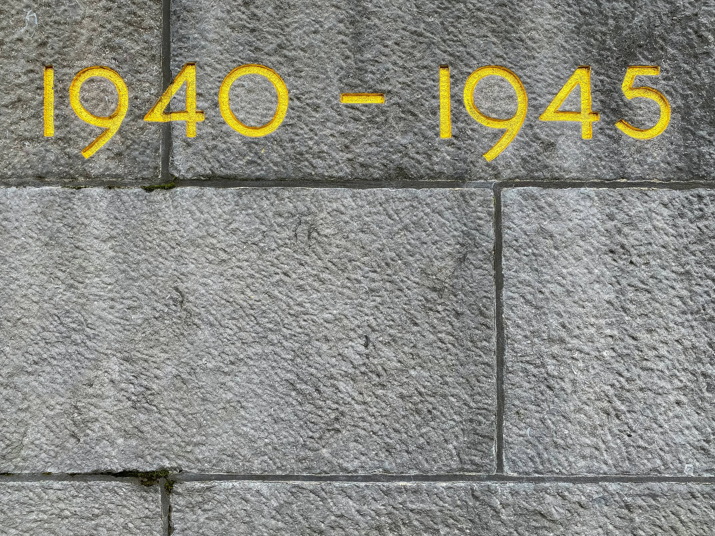 Remembrance 桌布 壁紙 — 風化灰色石塊的特寫，帶有粗體黃色油漆日期1940-1945，標誌著歷史時期。