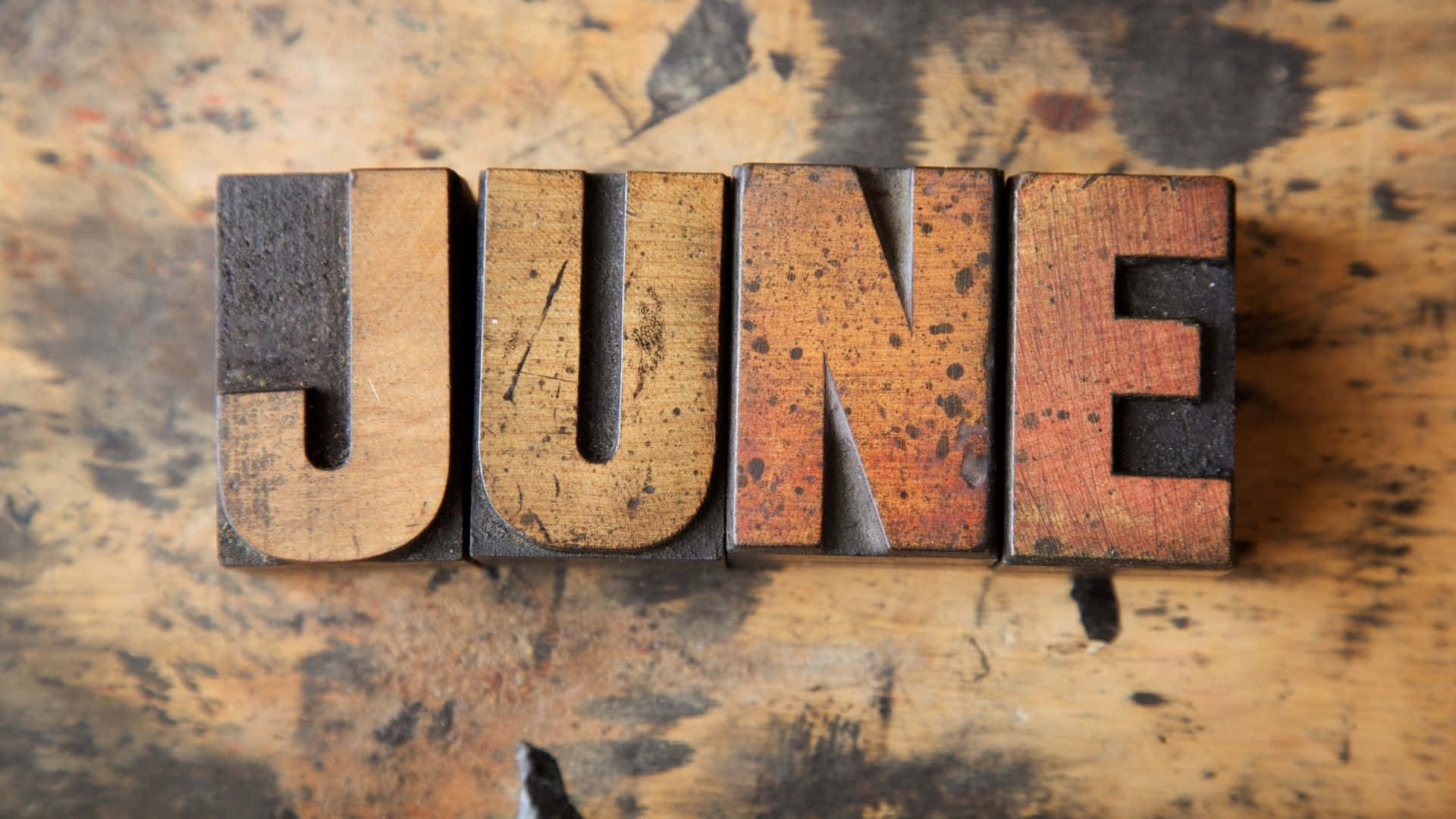 June 桌布 壁紙 — 風化的木製活字塊拼出JUNE，放在有污漬的工作檯面上。