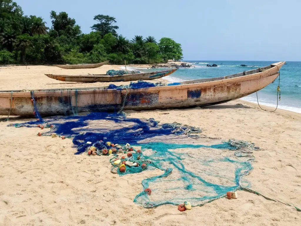 Liberia 桌布 壁紙 — 風化的木製漁船停泊在沙灘上，旁邊是碧綠的海水，背景有茂密的綠樹。