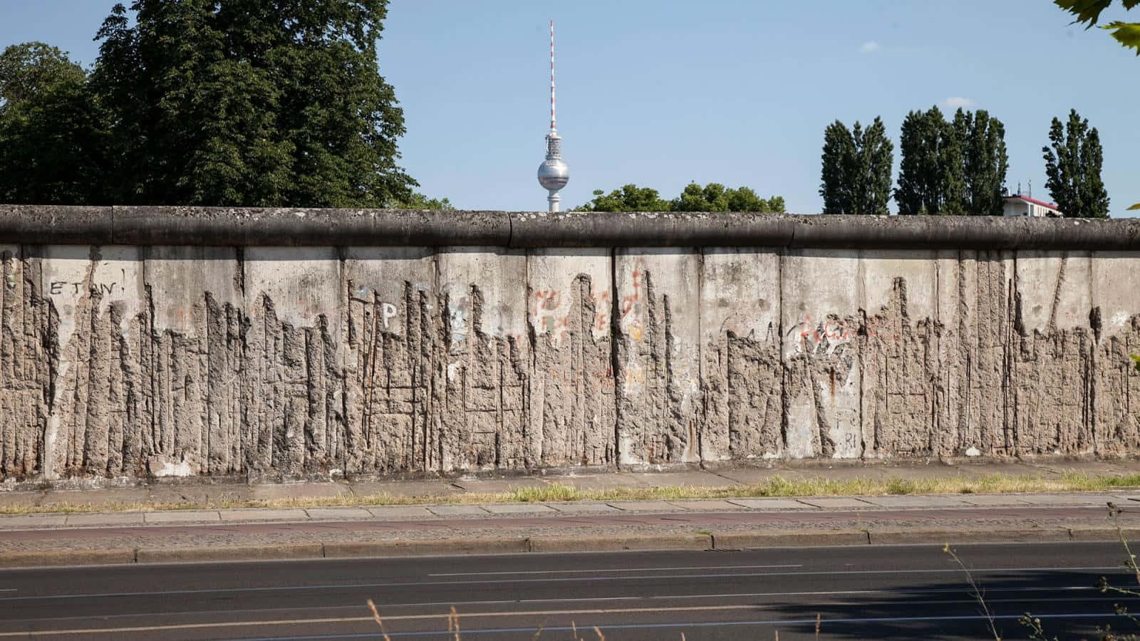 wall 桌布 壁紙 — 風化的柏林圍牆，帶有塗鴉和剝落的混凝土，背景是晴朗的藍天和電視塔。